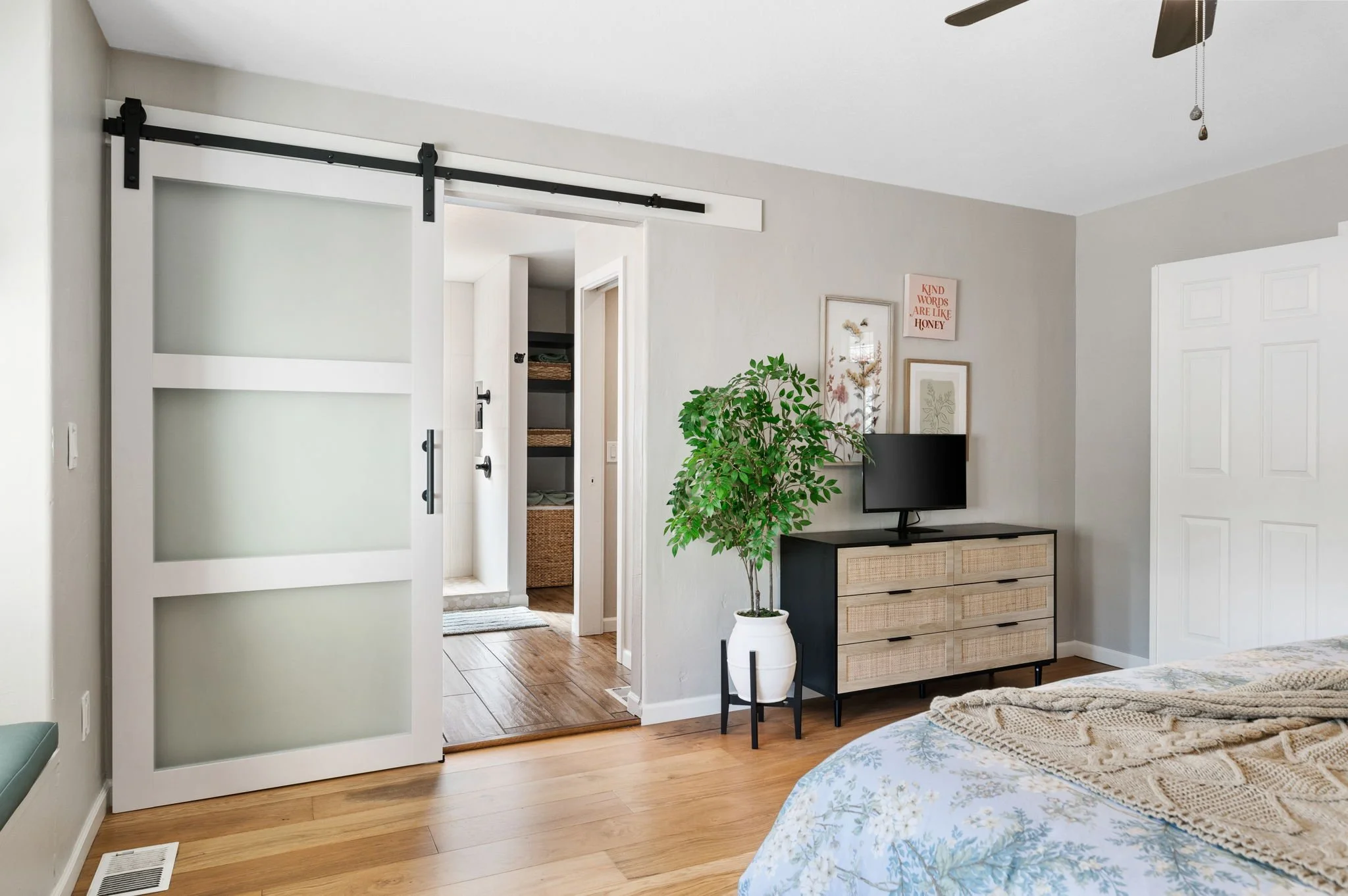Primary bedroom featuring a modern sliding barn door, warm wood flooring, natural wood furnishings, and soft neutral finishes.