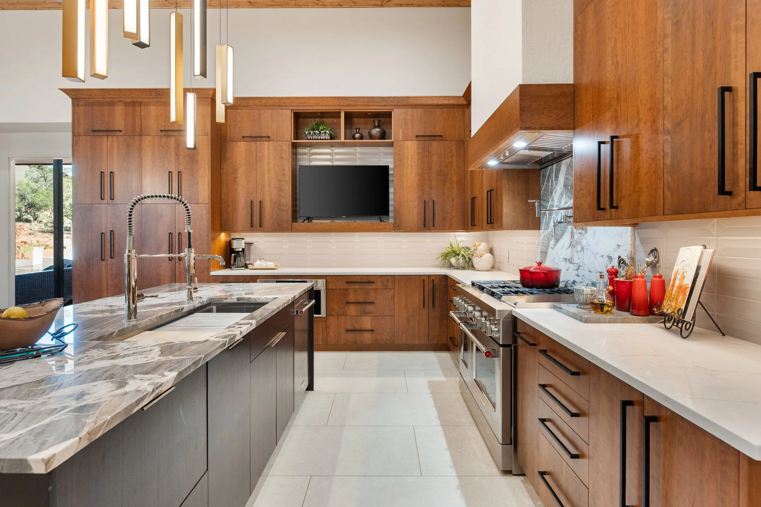 Warm contemporary kitchen featuring custom wood cabinetry, dramatic stone countertops, integrated appliances, and an expansive island designed for cooking, entertaining, and everyday gathering.