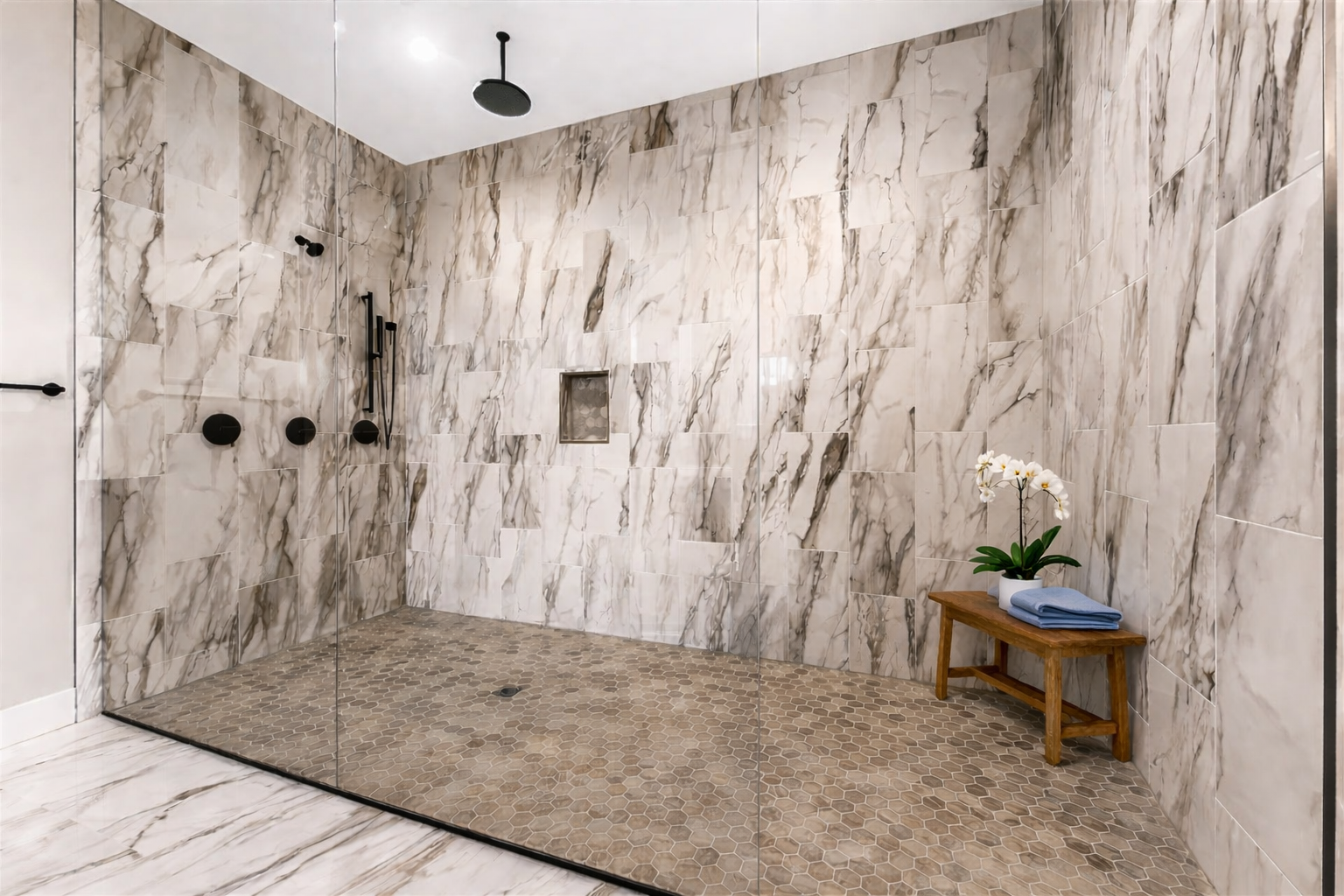Spa-inspired walk-in shower featuring floor-to-ceiling marble-look tile, frameless glass, matte black fixtures, and a built-in shower niche.