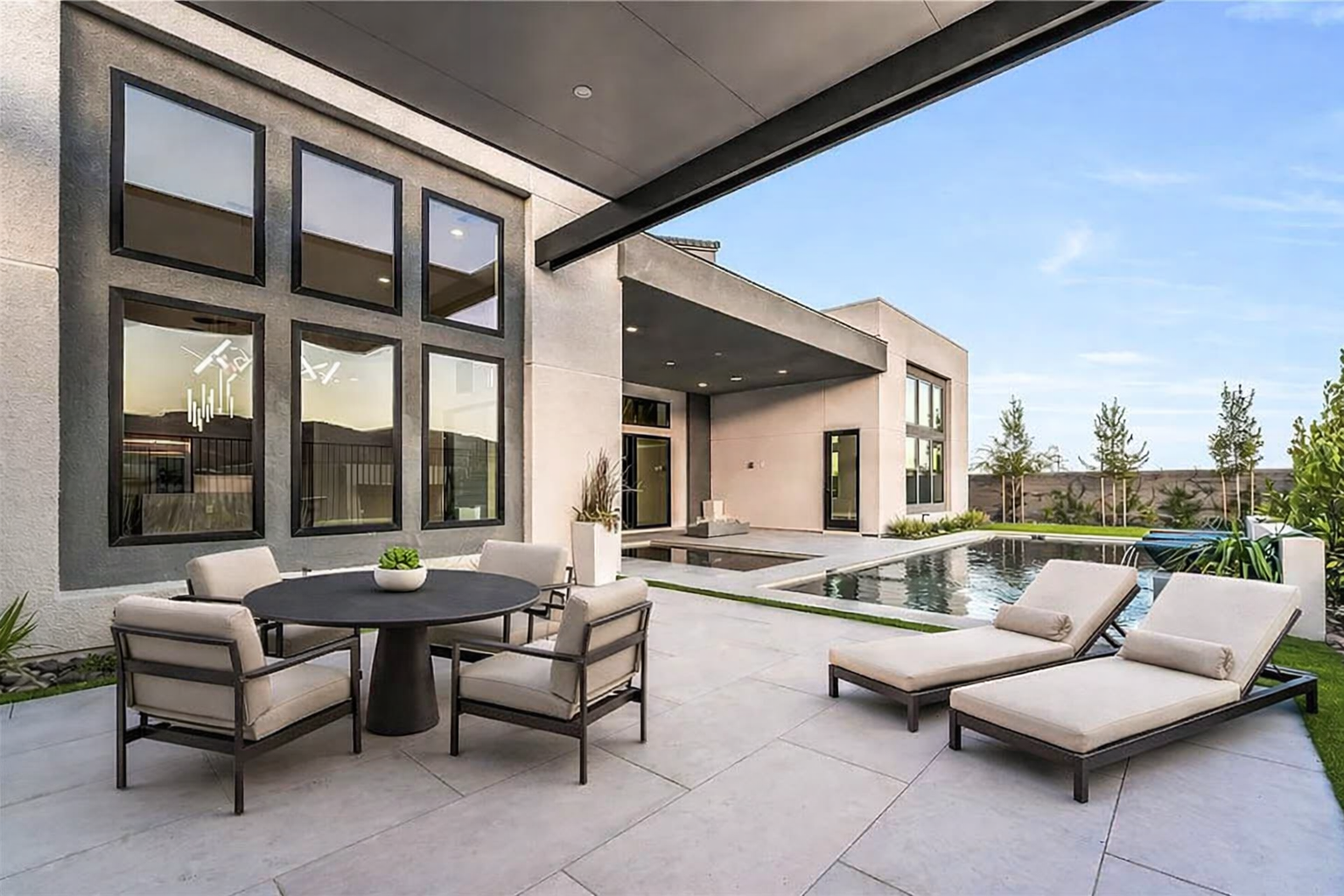 Contemporary outdoor living space featuring a covered patio, modern lounge furnishings, dining area, and a resort-style pool.