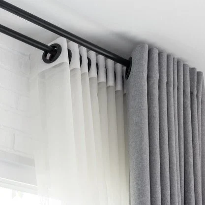 Close-up of a window with layered white and gray curtains hanging from a black curtain rod.