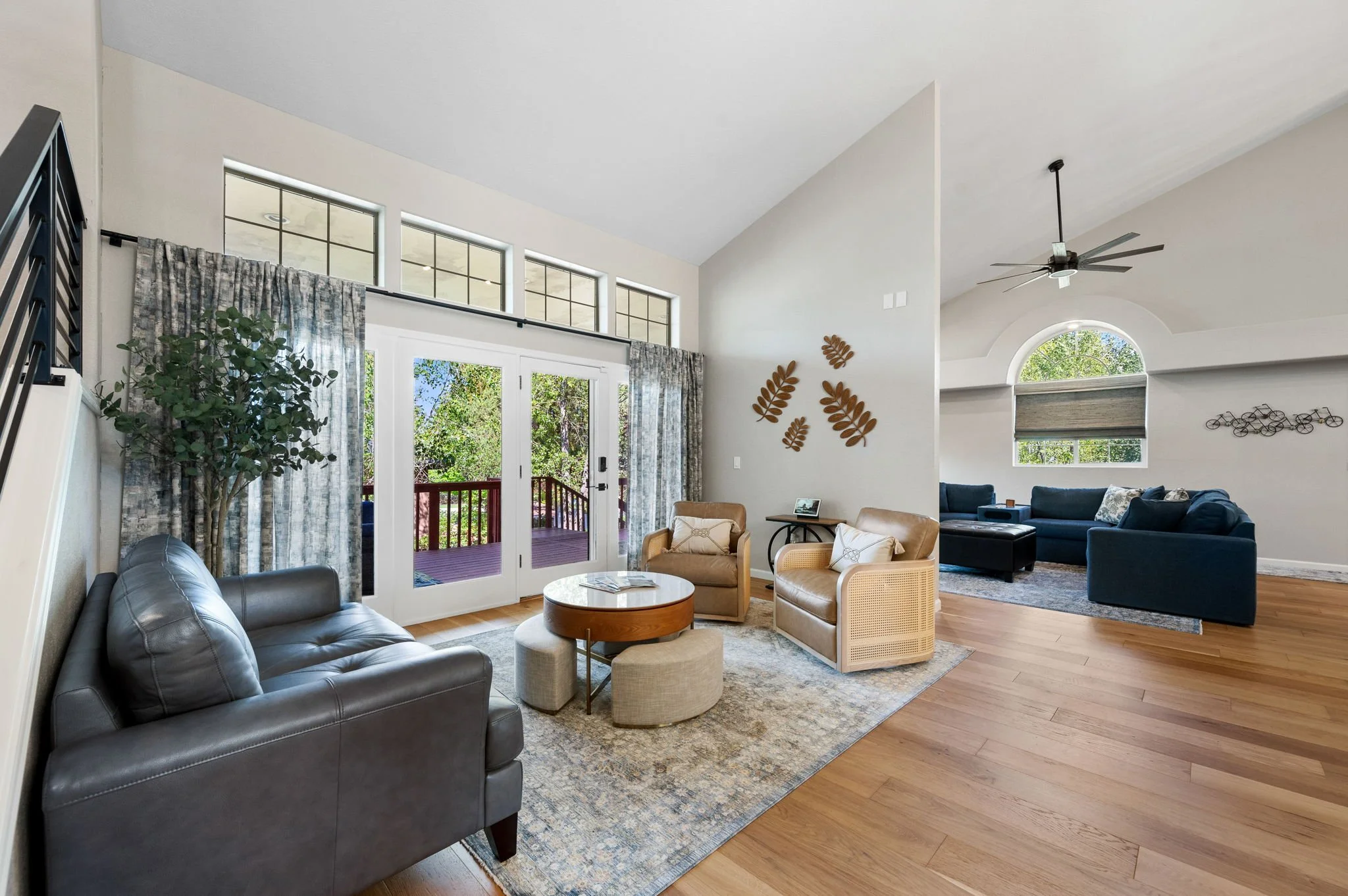 Light-filled living room featuring warm wood flooring, layered neutral furnishings, a textured area rug, and expansive windows overlooking the outdoor living space.