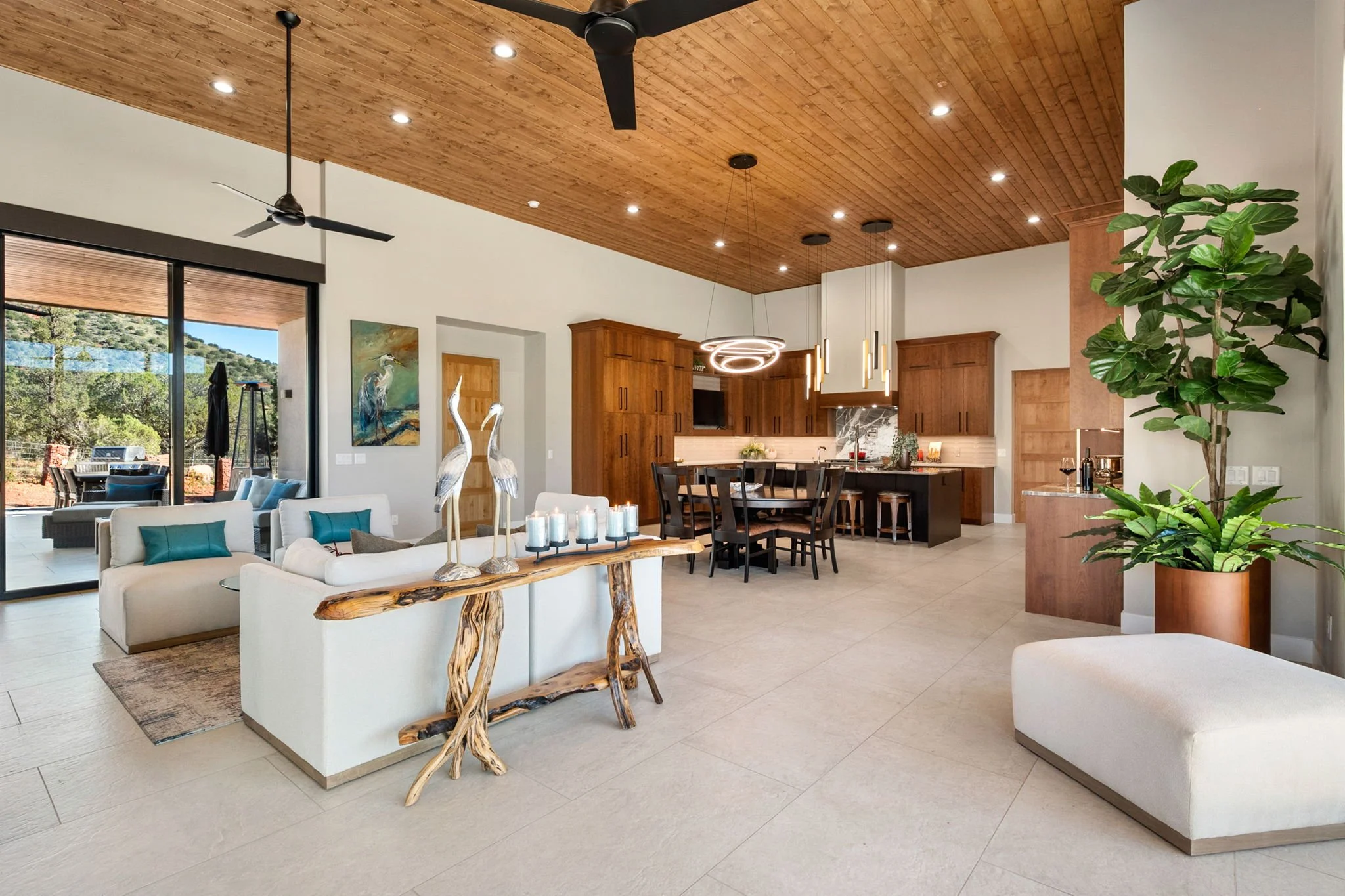 Open-concept great room featuring a warm wood-clad ceiling, expansive indoor-outdoor views, custom furnishings, layered lighting, and a seamless connection to the kitchen and dining spaces.