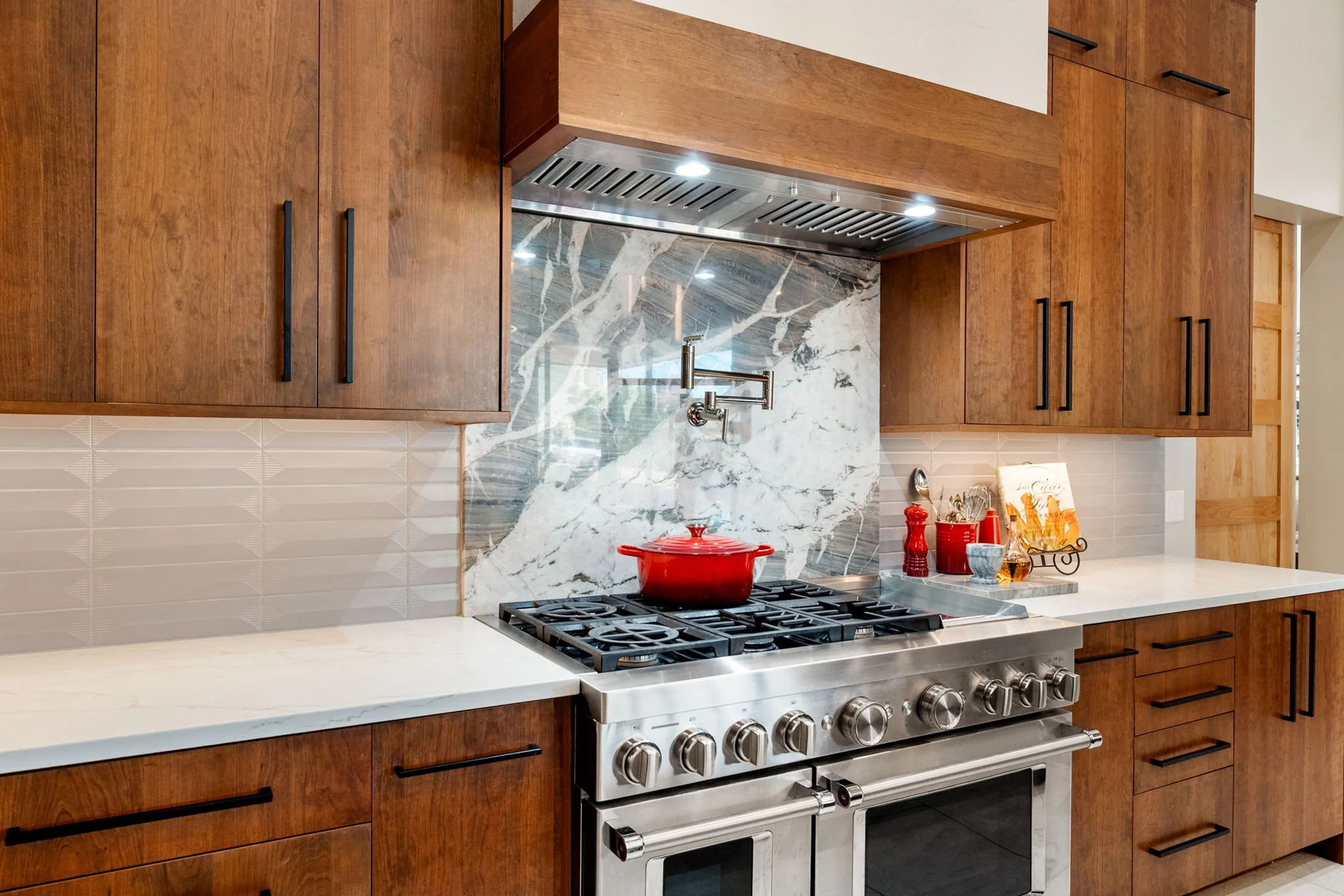 Custom wood cabinetry with professional range, sculptural stone backsplash, and warm modern finishes.