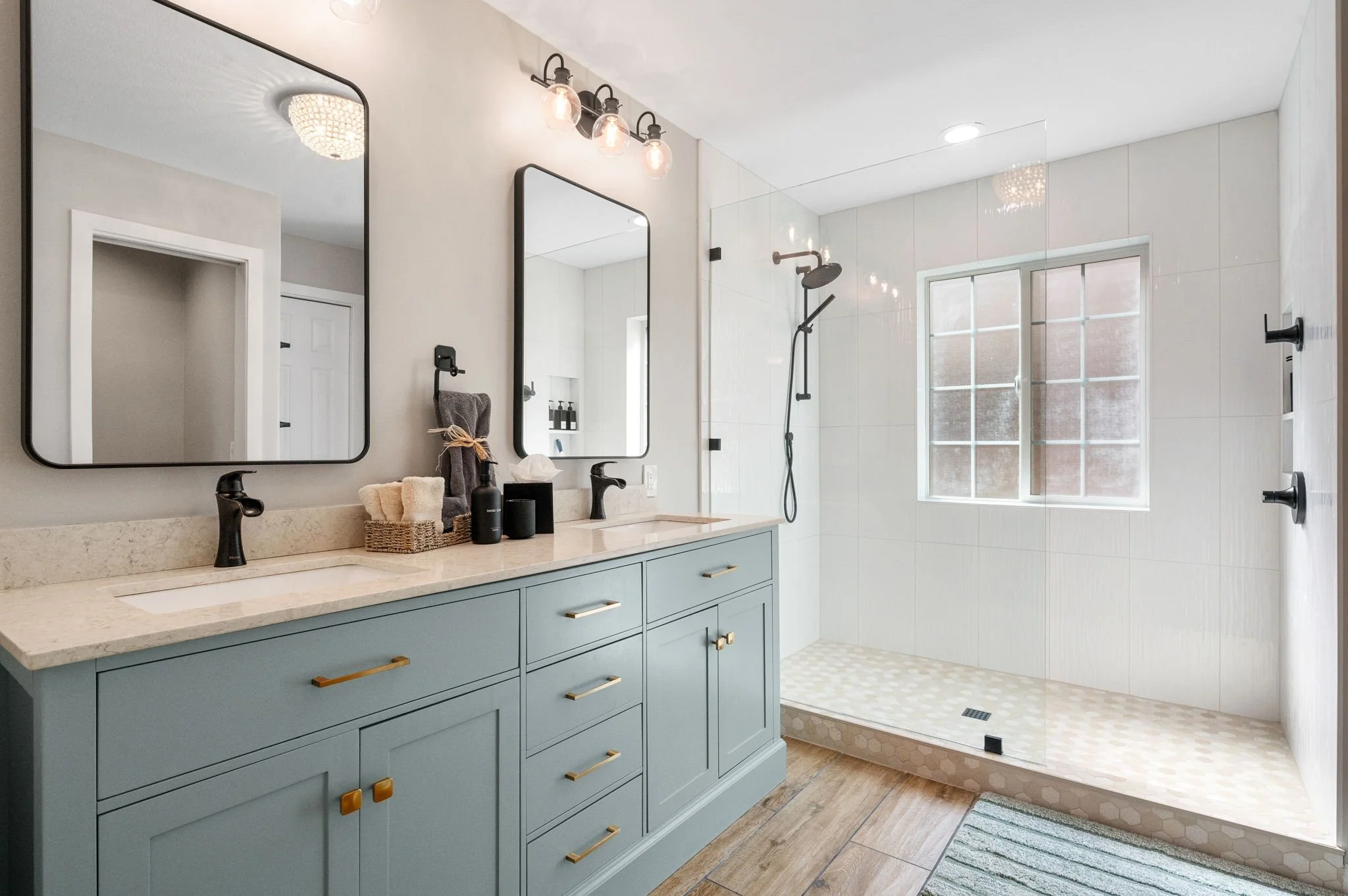 Updated bathroom featuring soft blue cabinetry, quartz countertops, matte black fixtures, dual mirrors, and a spacious walk-in shower.