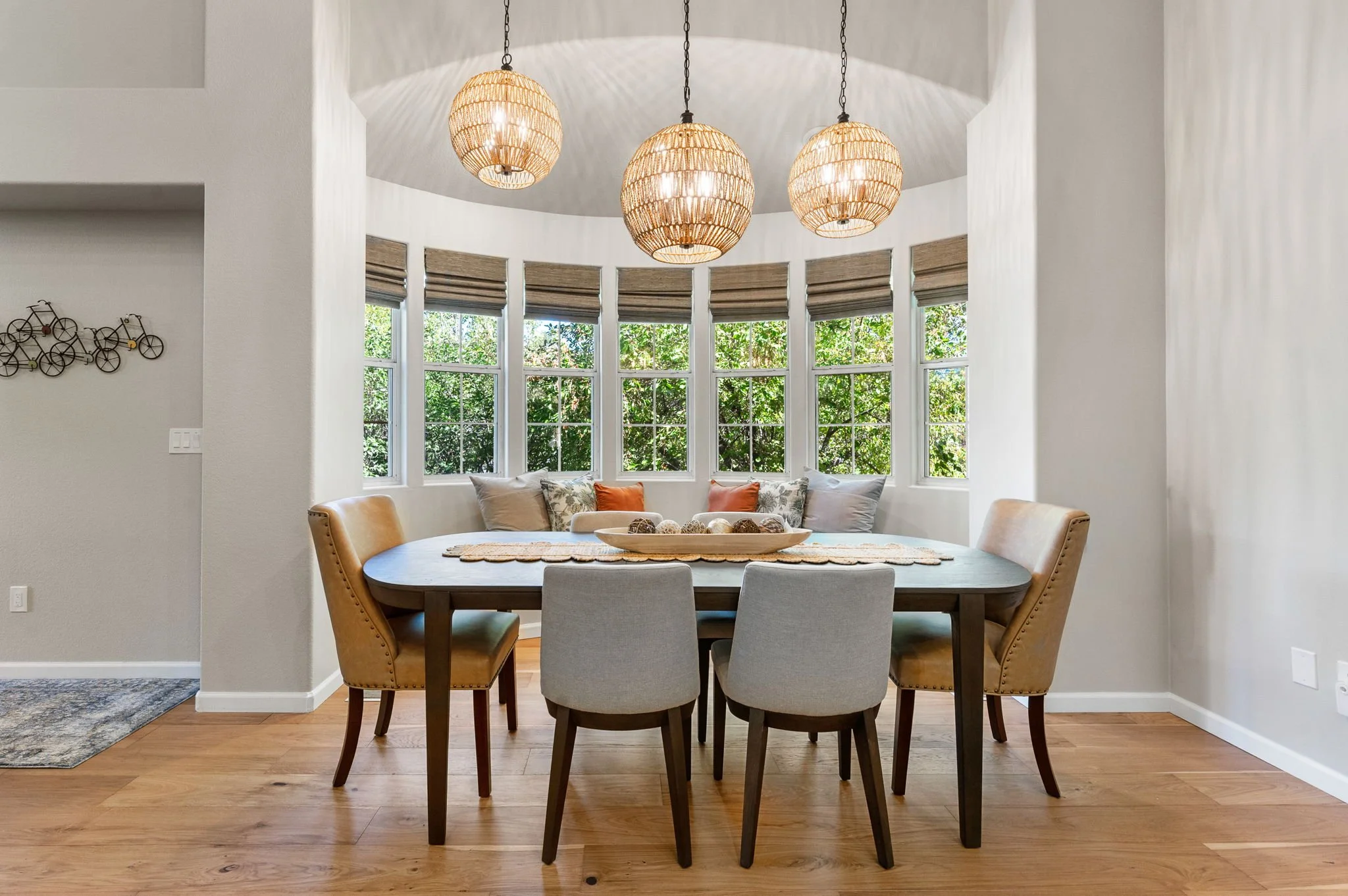 Inviting dining area featuring a bay of windows, warm wood flooring, upholstered dining chairs, and sculptural pendant lighting.