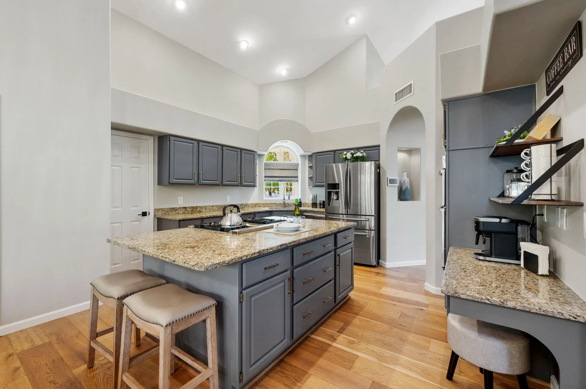 Transitional kitchen featuring gray cabinetry, granite countertops, a spacious center island, warm wood flooring, and arched architectural details.