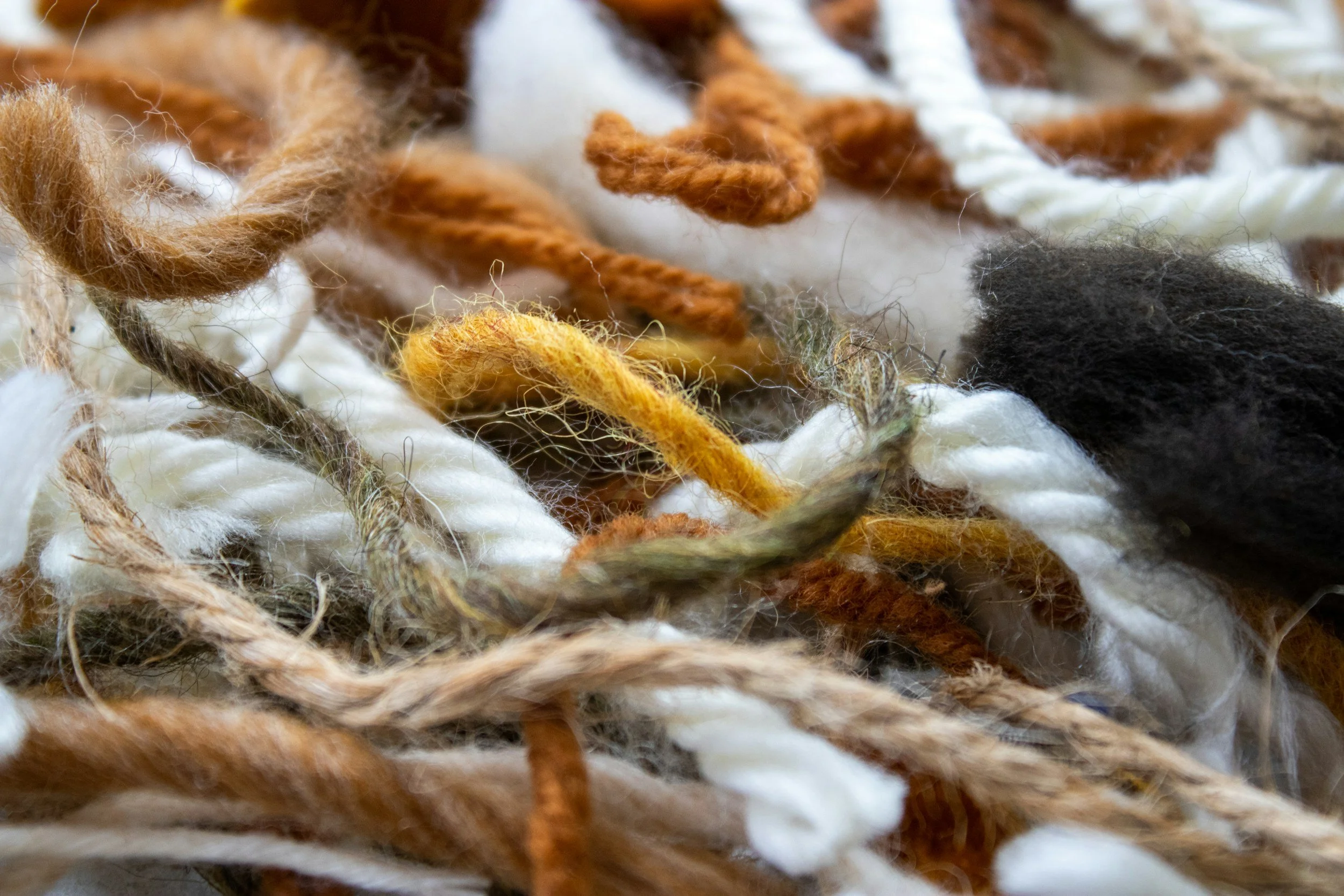Close-up of multicolored yarns in shades of brown, white, yellow, black, and cream intertwined and textured.