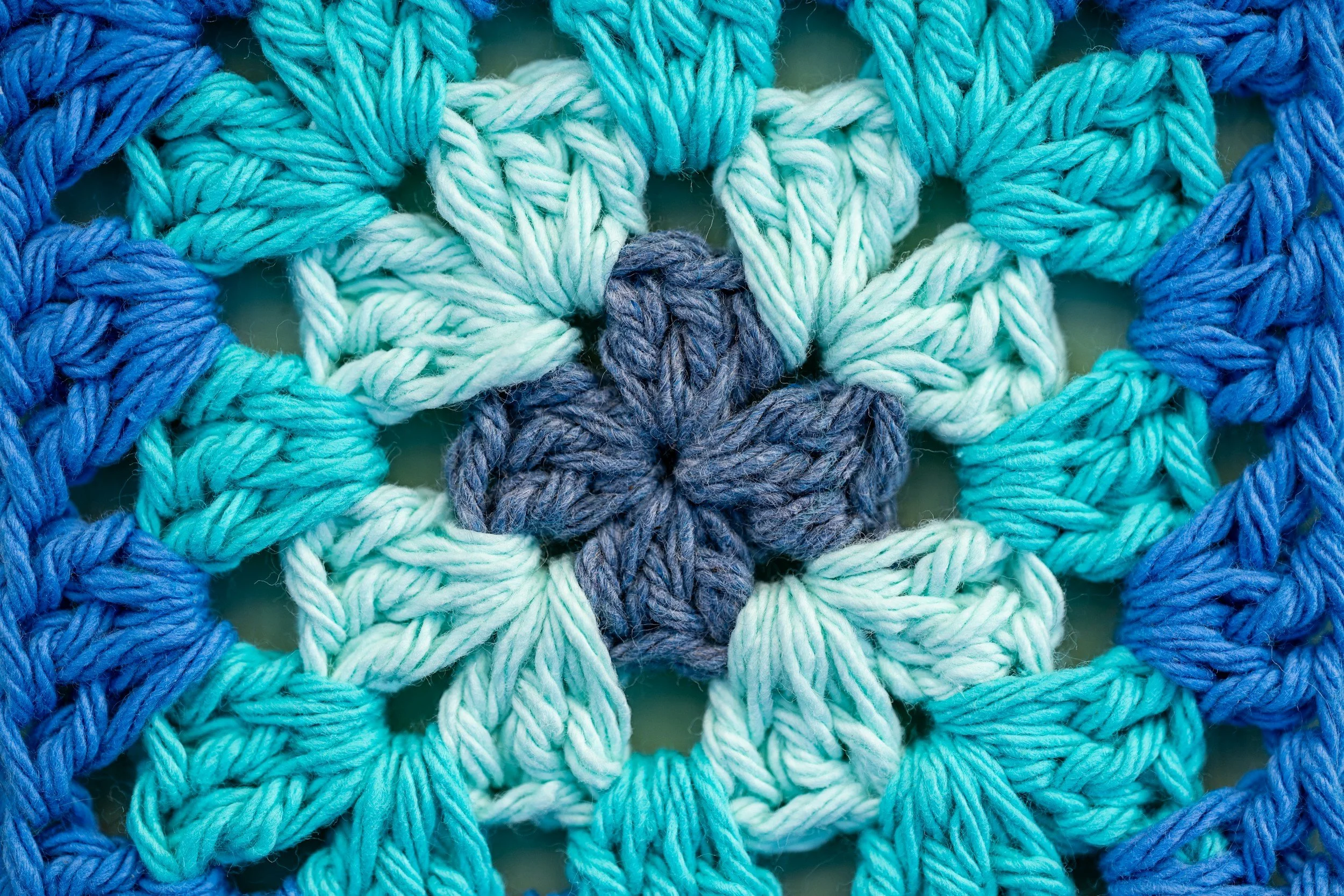 Close-up of a crochet project made with various shades of blue and teal yarn, showcasing a textured pattern.