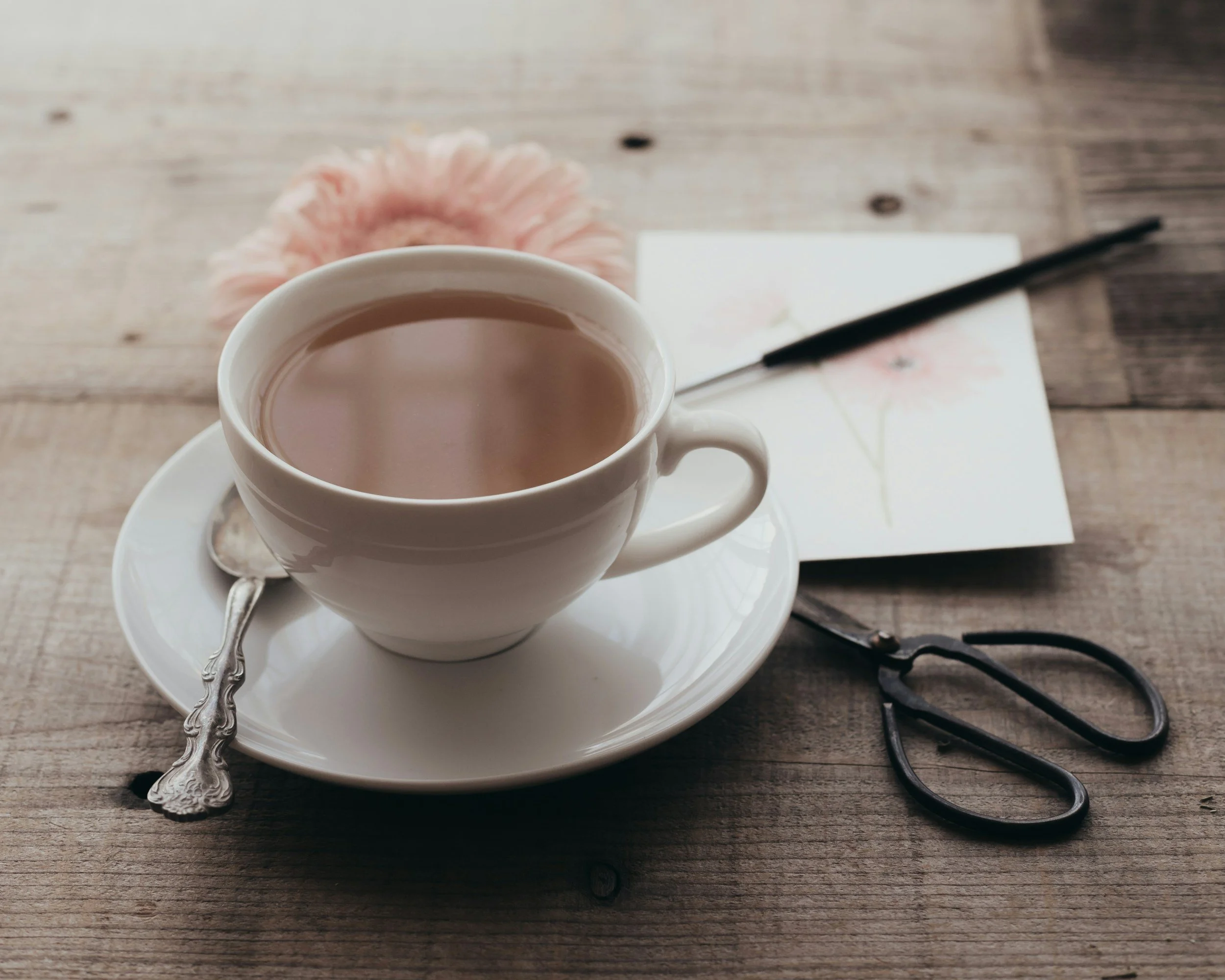 A cup of tea sits on a crafting table with a flower and a drawing of it, along with various tools.