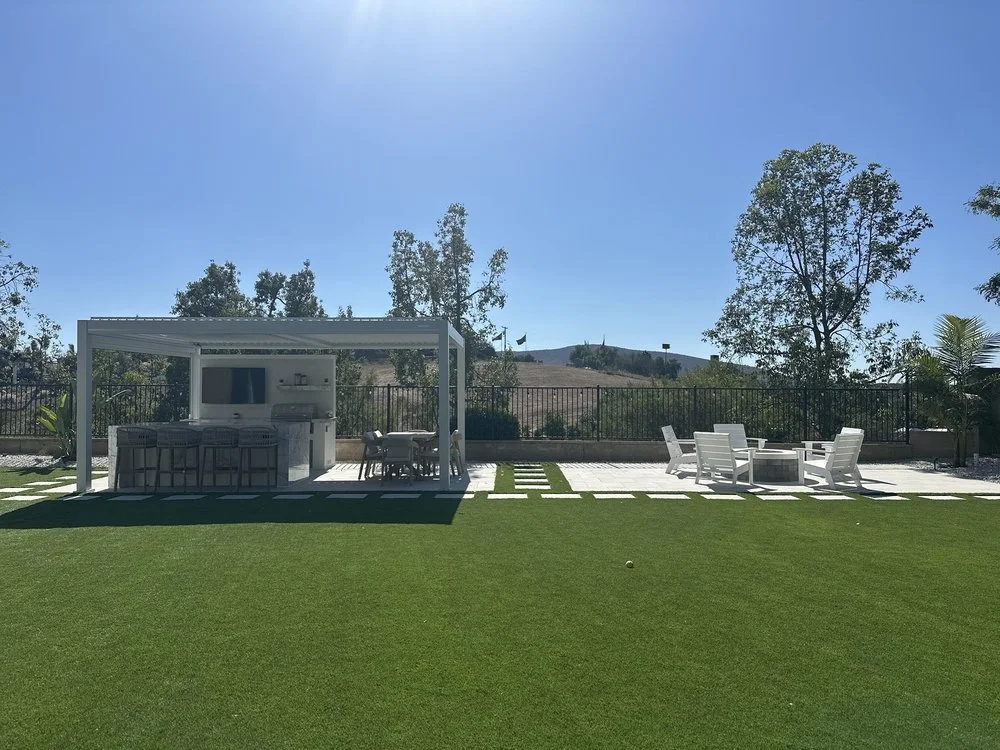 Complete outdoor remodel featuring artificial turf, porcelain pavers, stepping stones, a custom fire pit, gas line installation, electrical setup for a prebuilt outdoor kitchen, and installation of a prebuilt pergola.  