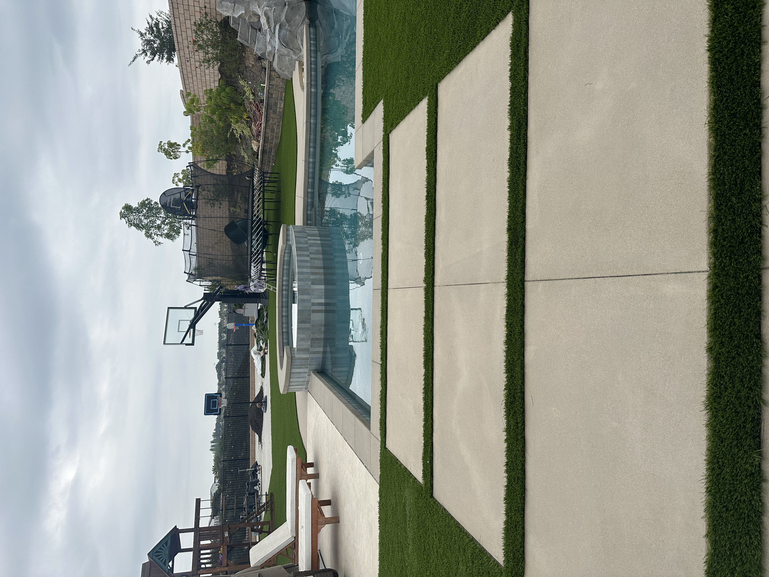 Concrete stepping stones, artificial turf, and pool coping installation for a clean, modern backyard finish.
