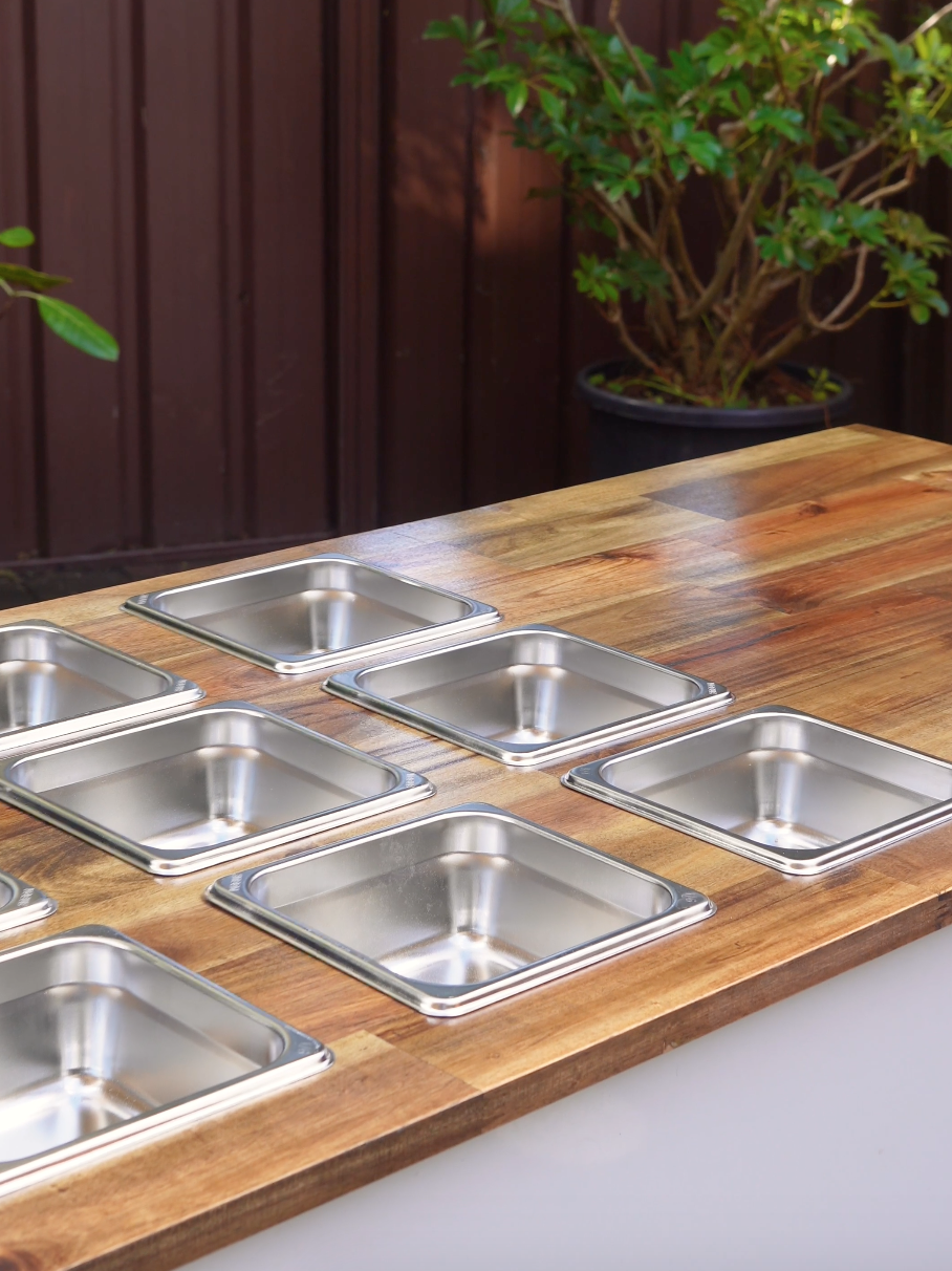 Event car with stainless steel food pans on a wooden countertop, suitable for charcuterie, lollies and other snacks