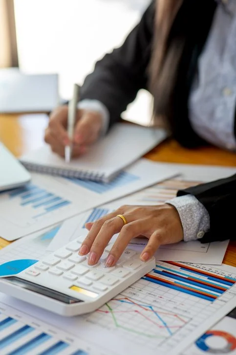 Person using a calculator on financial documents with charts and graphs at a desk.
