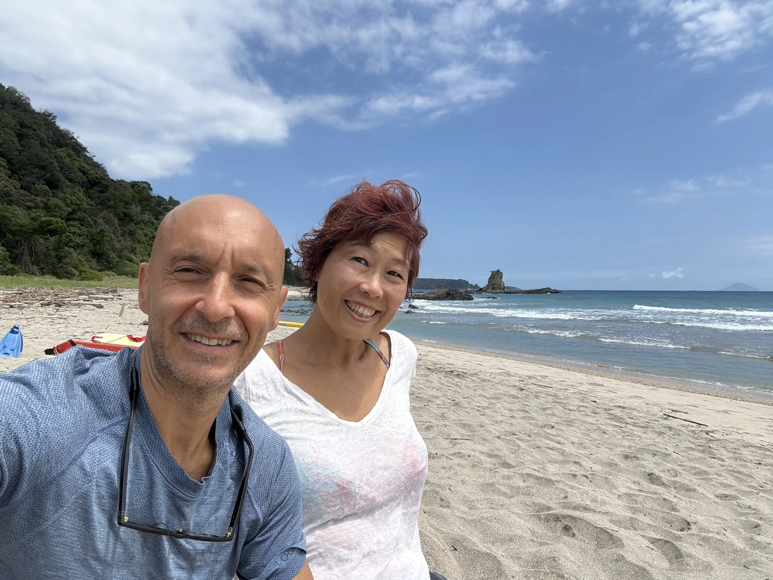 ビーチで笑顔の男女の写真。青い空と海、遠くに岩礁が見えるビーチ風景。