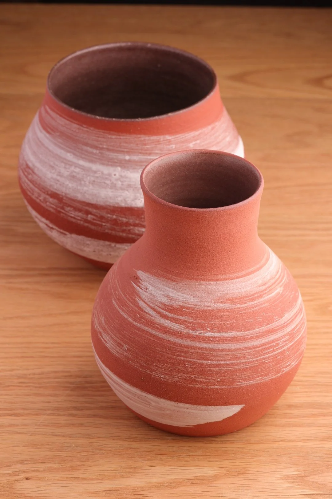 茶色と白の縞模様の陶器の花瓶が二つ、木製のテーブルの上に置かれている