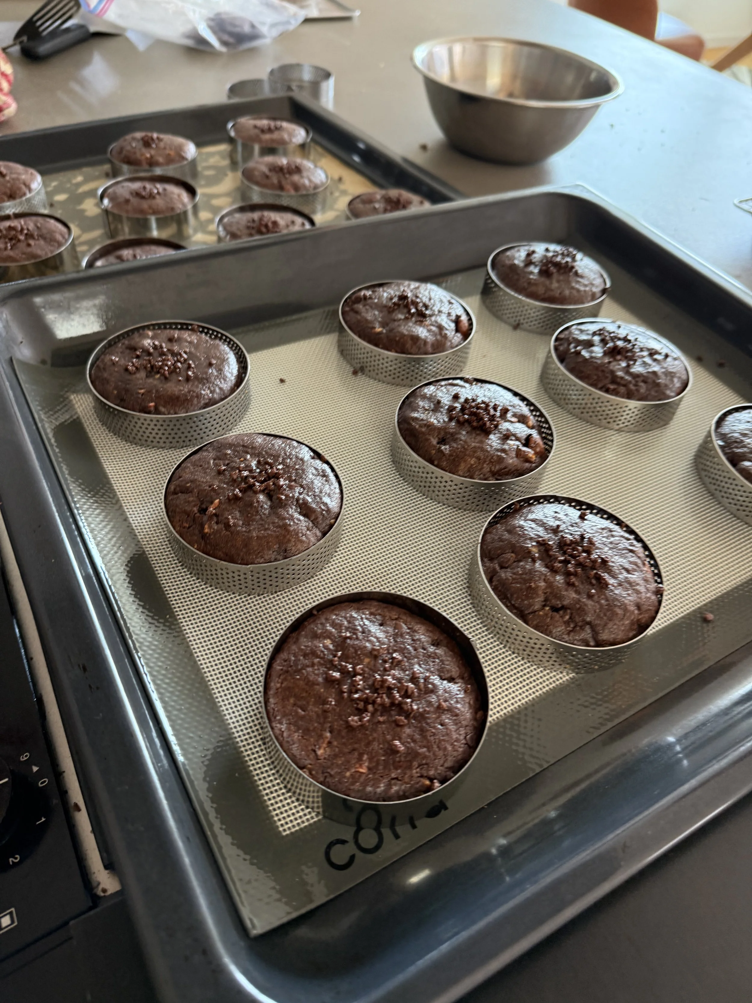 オーブンで焼かれているチョコレートブラウニーのカップケーキの写真。複数のブラウニーが金属の型に入っている。
