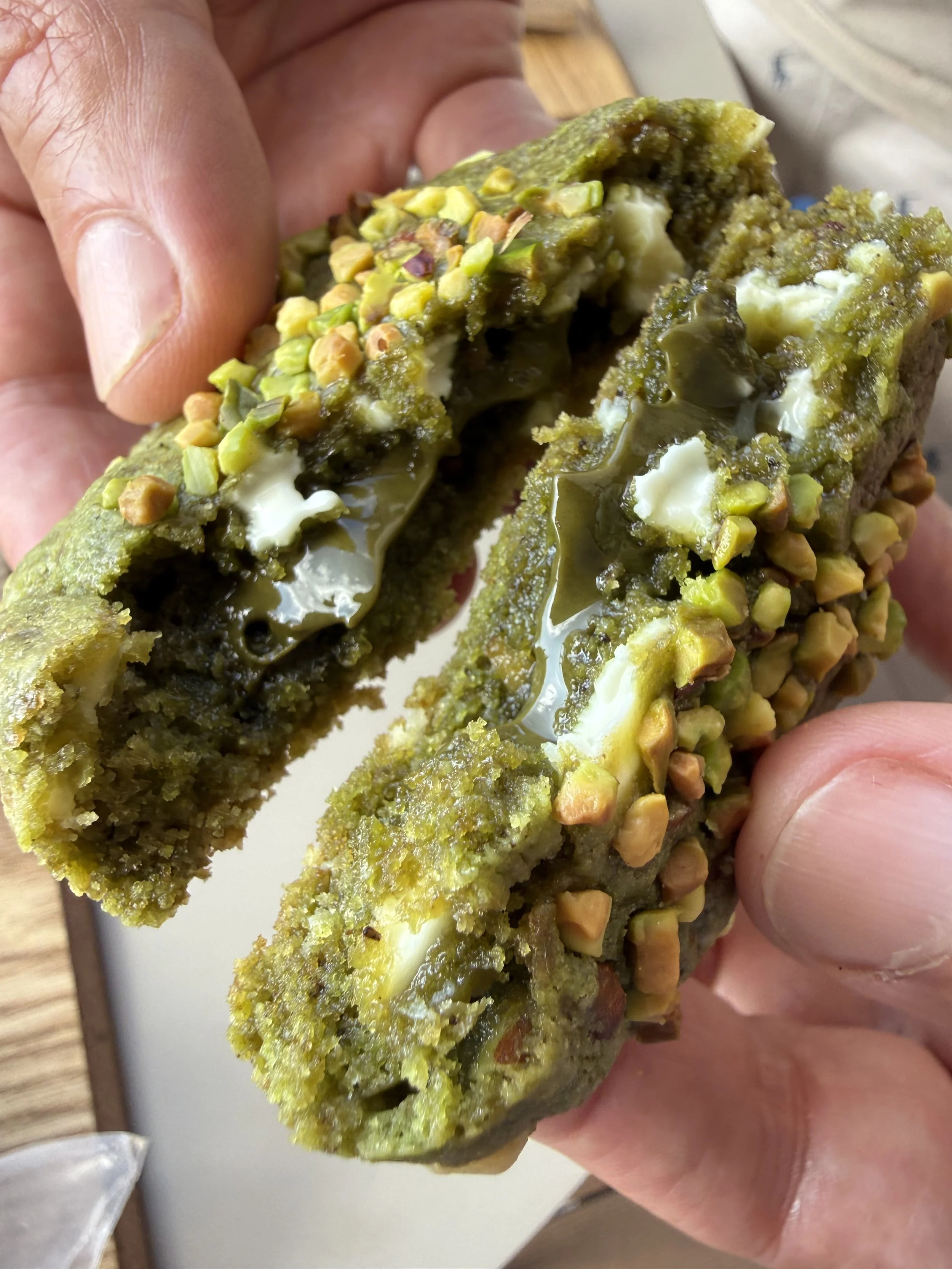手で持っている抹茶味のケーキの断面。上には刻んだナッツがトッピングされている。中はクリームと苔のような緑色のケーキ層。