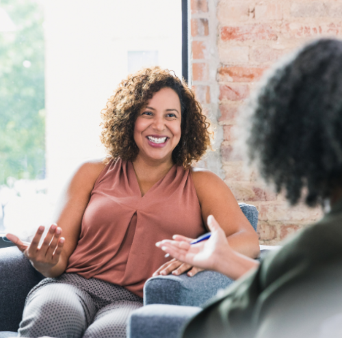 Woman smiling and speaking during a conversation with another person in a bright indoor setting.