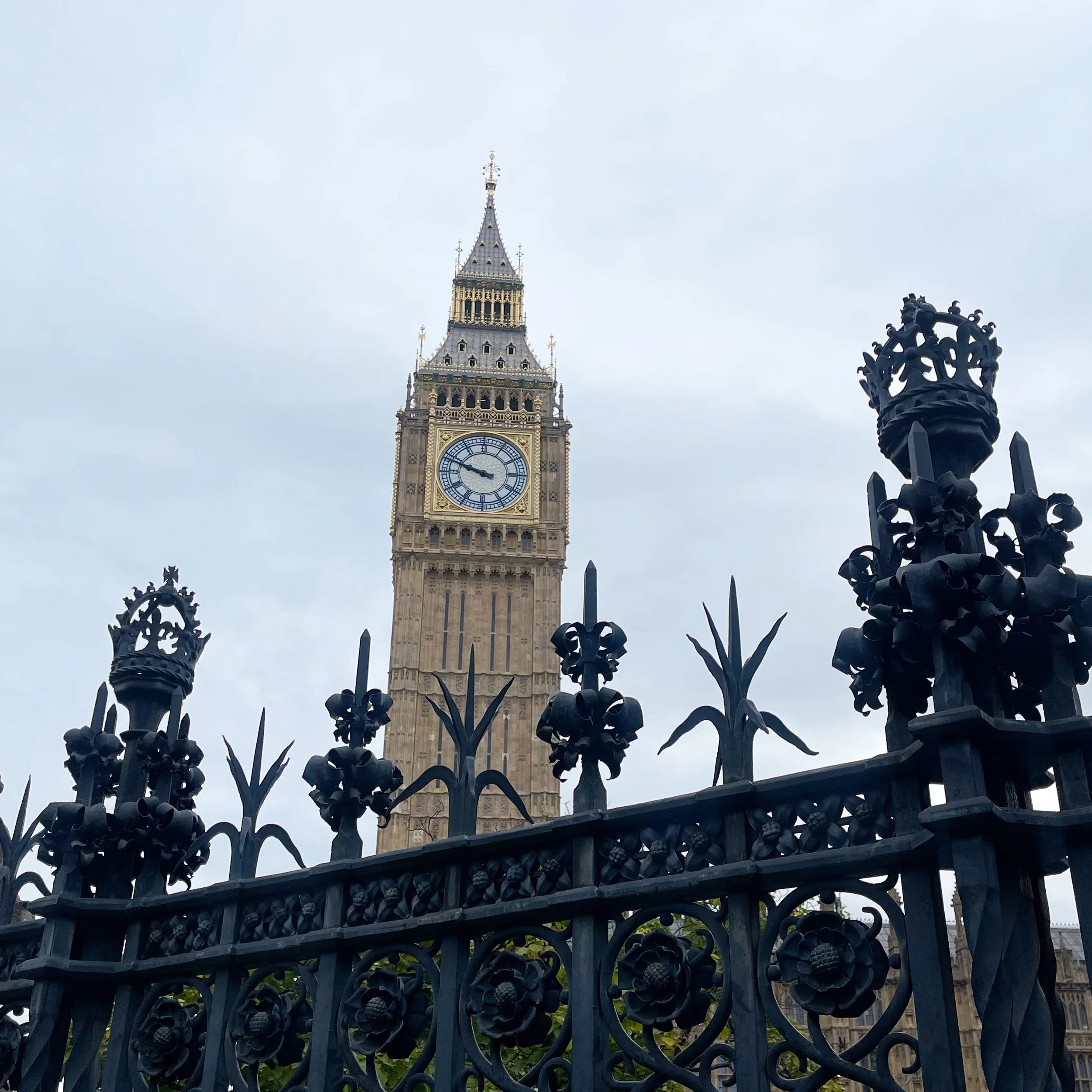 Big Ben behind a black ornate fence with decorative finials, overcast sky in London, UK