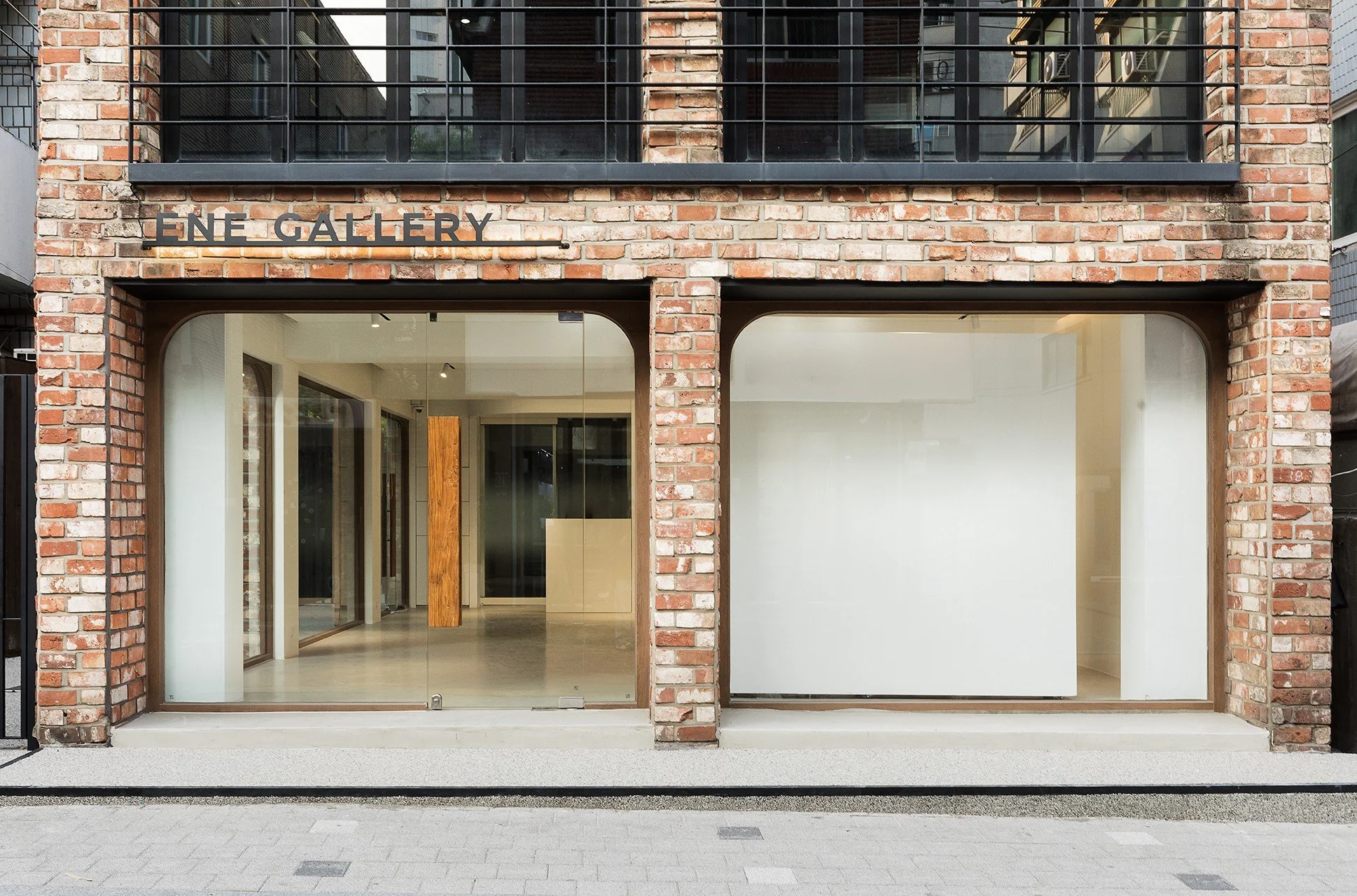 Exterior view of an art gallery storefront with large glass windows and brick walls, showcasing an interior with modern design and a wooden door.