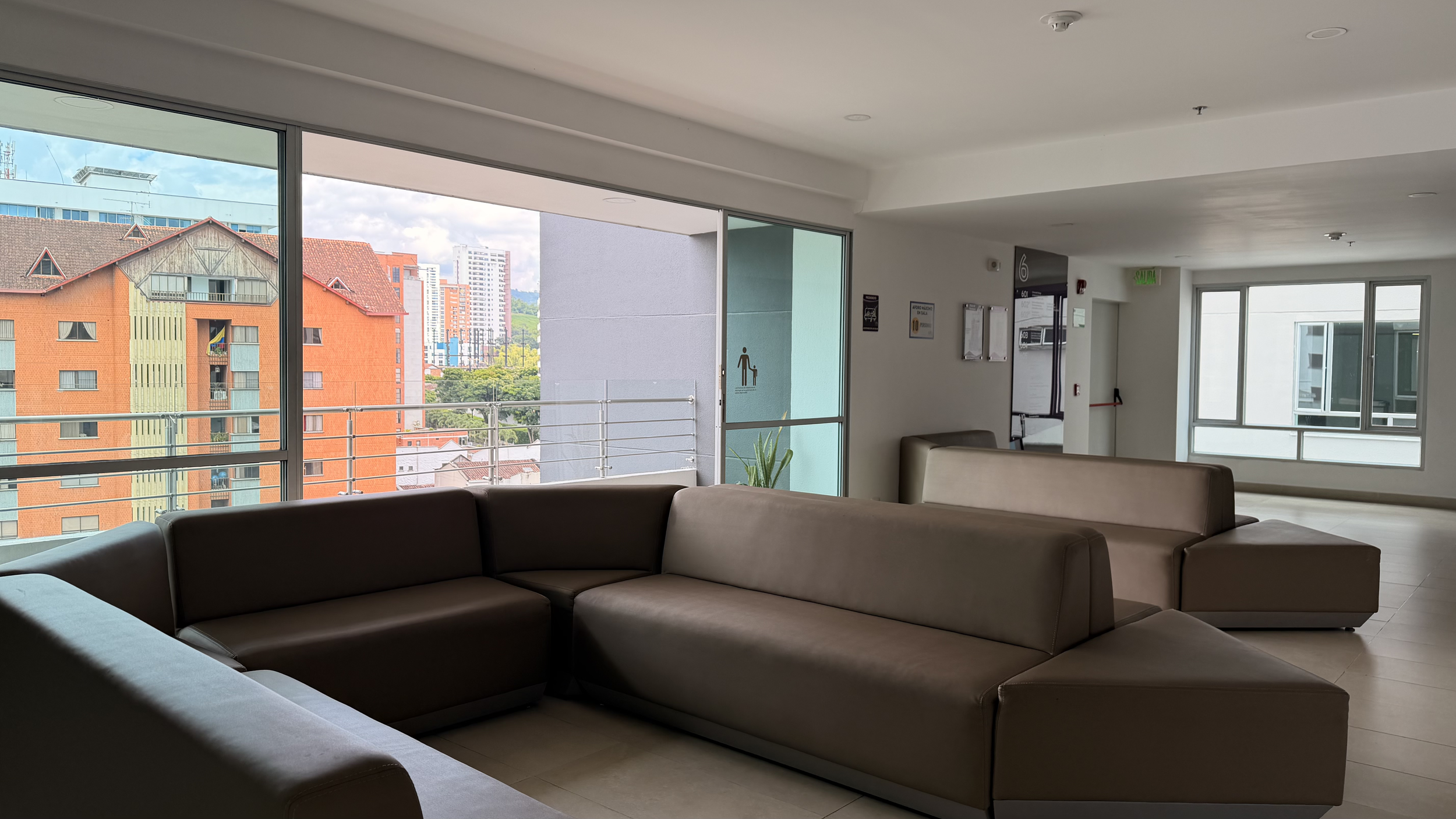Indoor lounge area with large windows showing apartment buildings and a cityscape in the background.