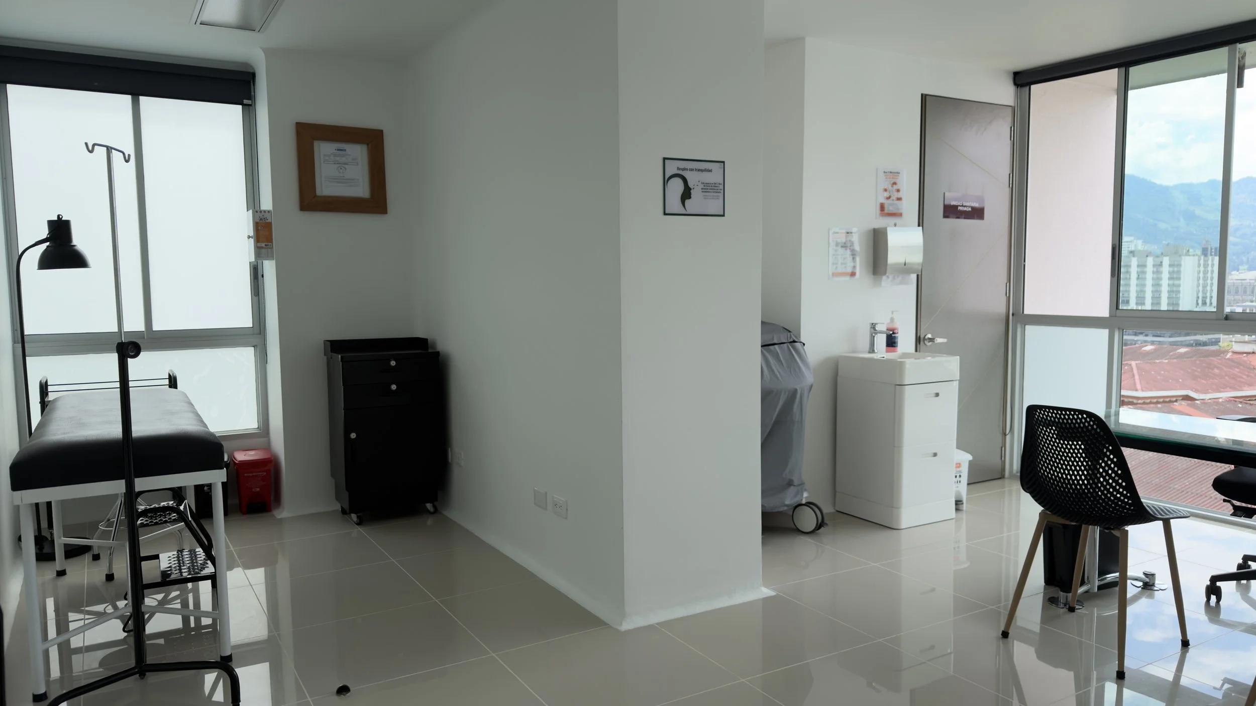 Hospital room with a window, medical equipment, and a small table with a chair.