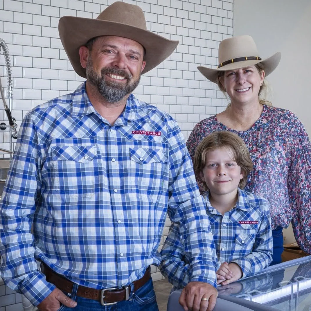 A family of four dressed in plaid shirts and cowboy hats standing in a kitchen with a white brick wall behind them.