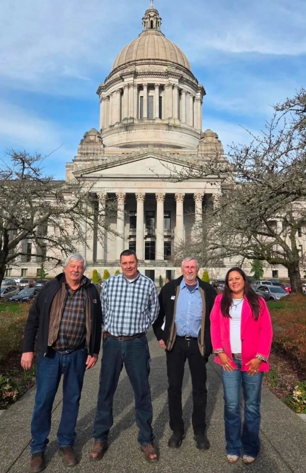 Four people standing in front of the Washington state capitol building, on a clear day with trees around.