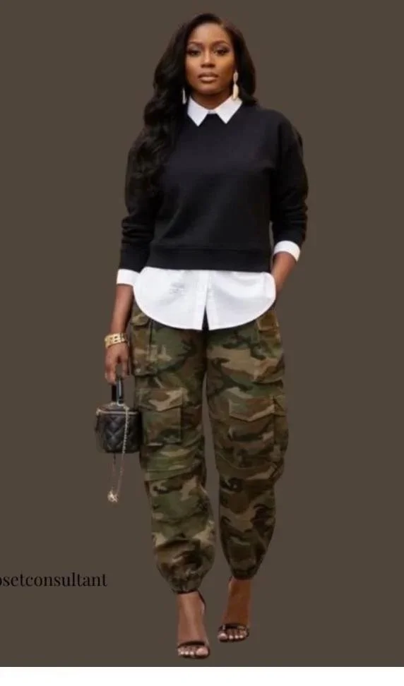Woman with long black hair wearing a black sweater over a white collared shirt, camouflage cargo pants, high heels, and holding a small purse.