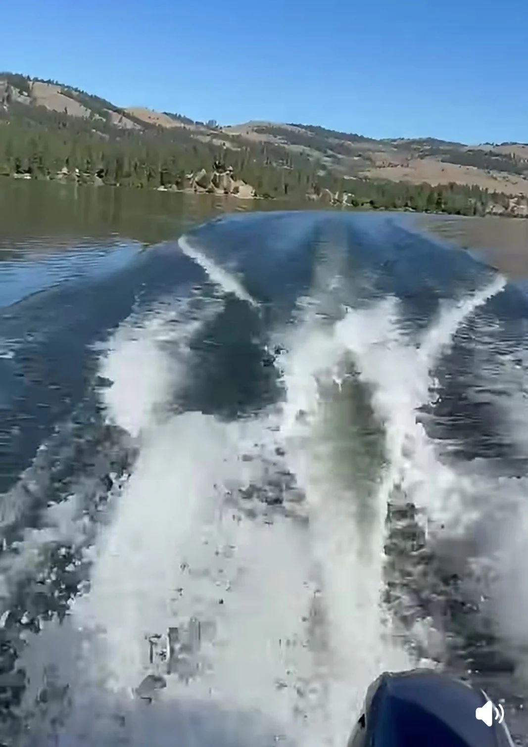 View from a boat showing water wake with mountains and trees in the background.