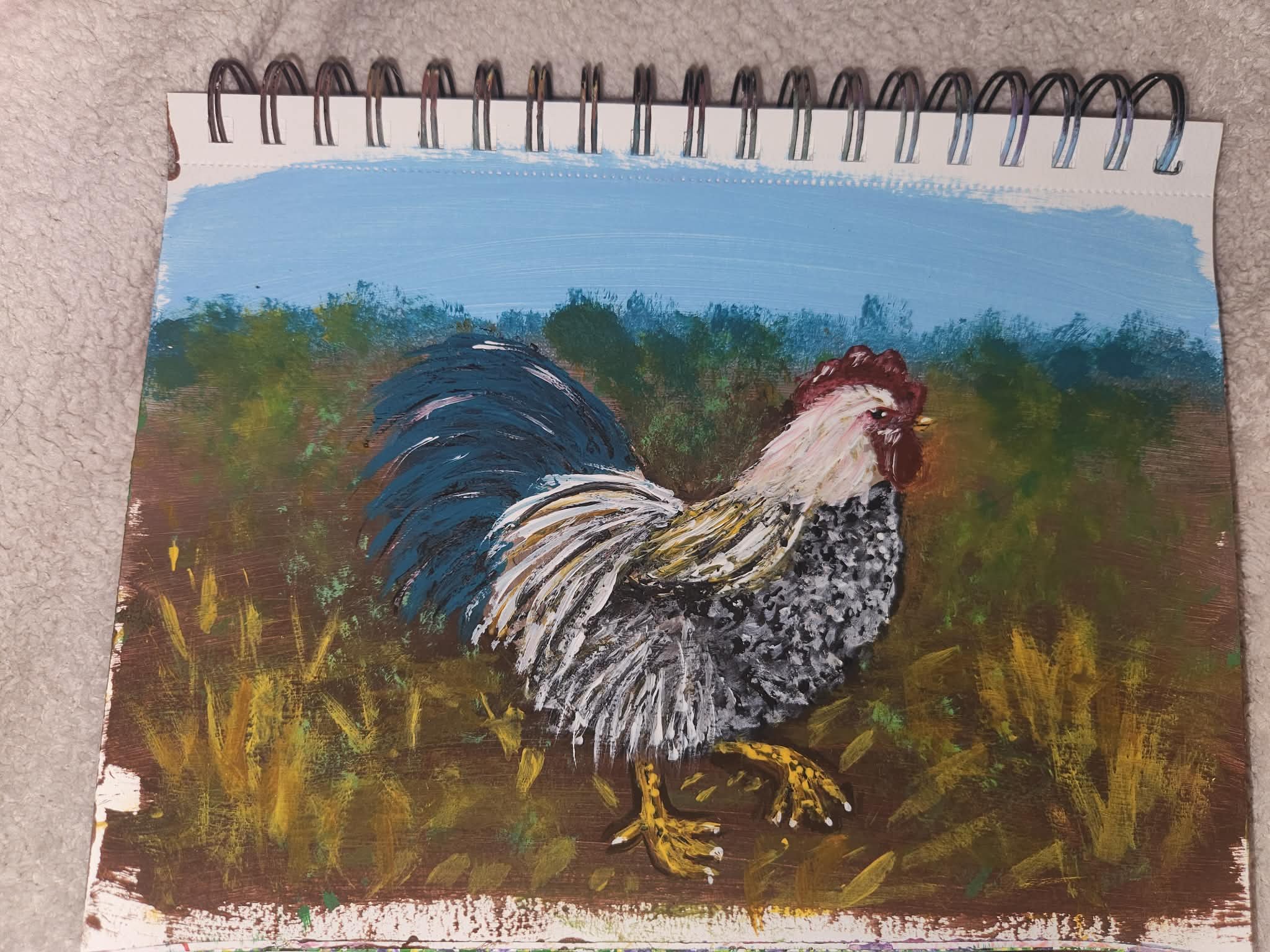 Original painting. A painting of a rooster standing on the ground with green and yellow grass, against a background of blue sky and trees.