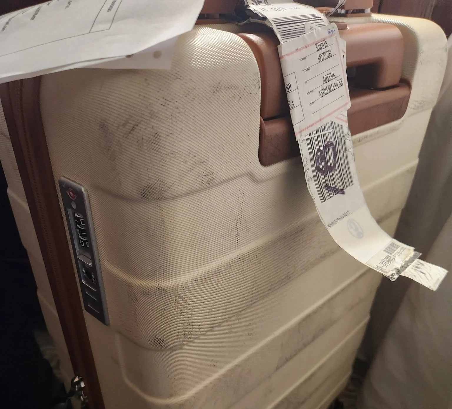 Beige hard-shell suitcase with a luggage tag and baggage receipt attached.