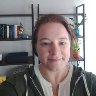 A photo of Liz Froment wearing a green top in front of a bookcase.