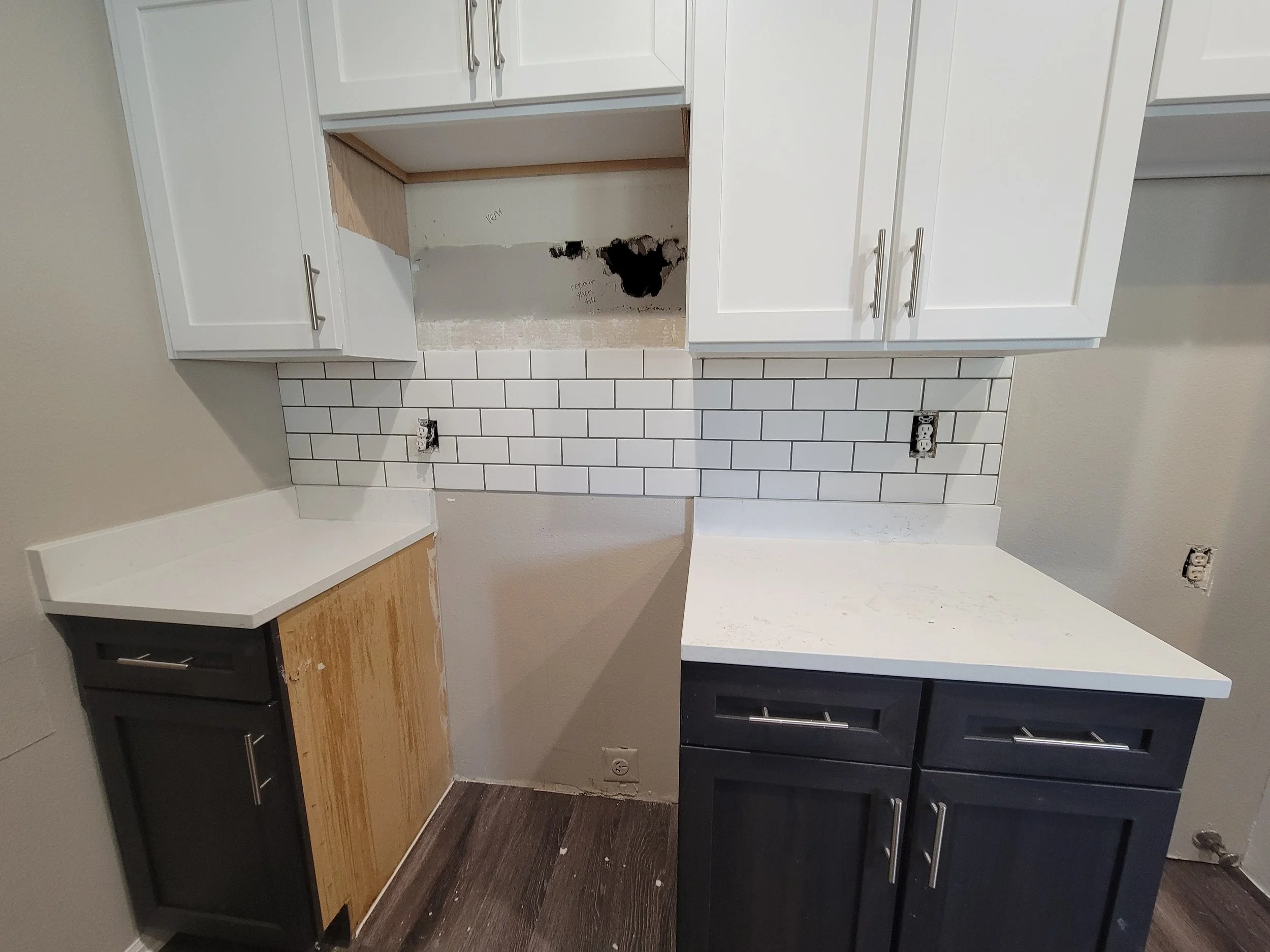 Kitchen cabinets and countertops with missing appliances and a white subway tile backsplash.