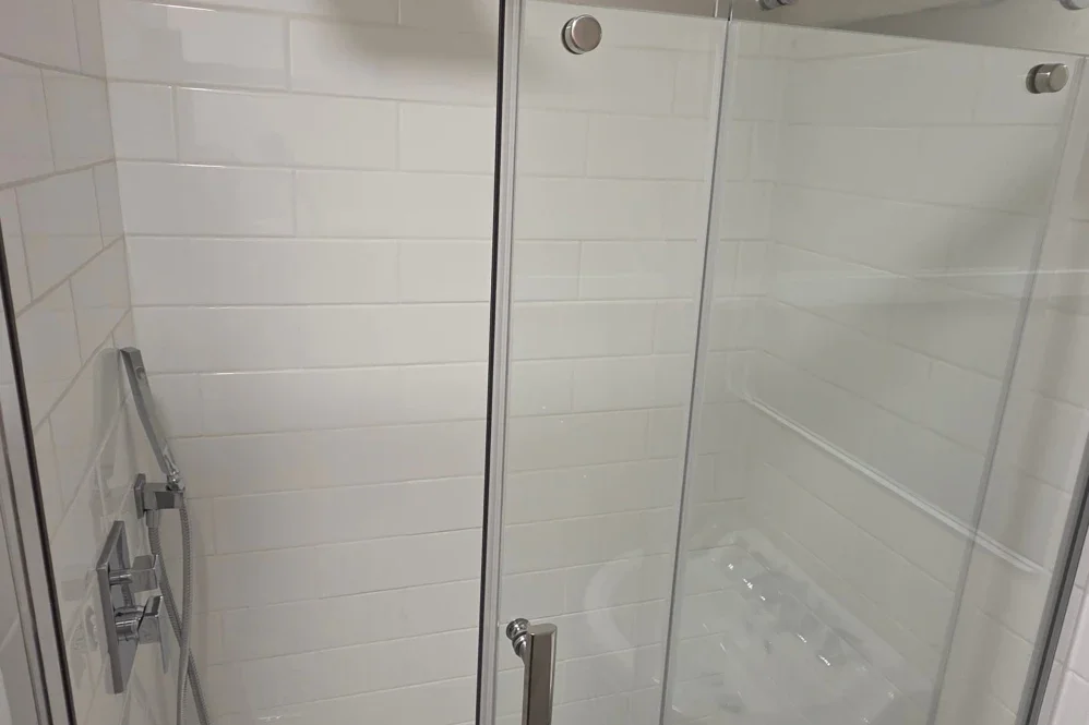 Empty glass shower enclosure with white tiled walls and a handheld showerhead