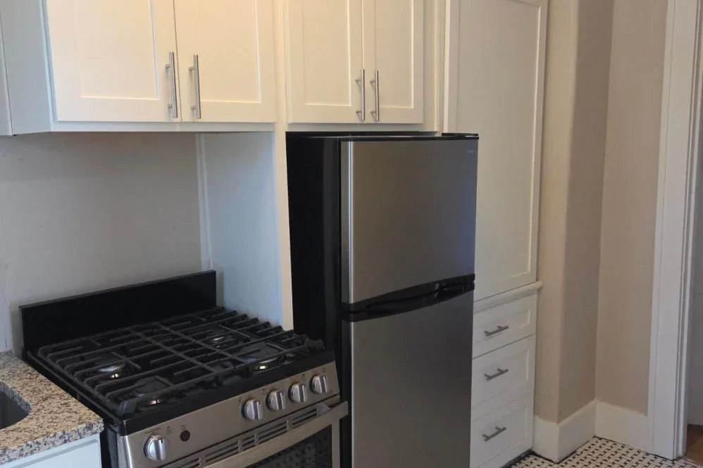 Kitchen with white cabinets, a black and stainless steel refrigerator, a stainless steel gas stove, granite countertop, and a tile floor.