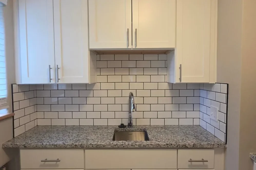 Kitchen with white cabinets, a granite countertop, a stainless steel sink, and white subway tile backsplash with black grout.
