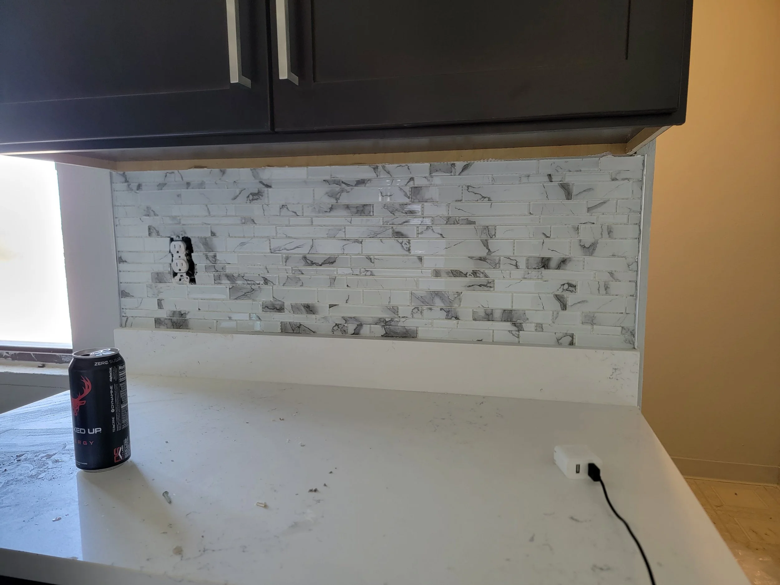 A kitchen countertop with a marble backsplash, a black can of energy drink, and a white outlet on the wall.