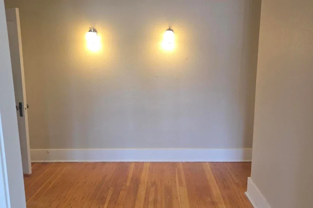 Empty room with two wall-mounted lights and a hardwood floor.