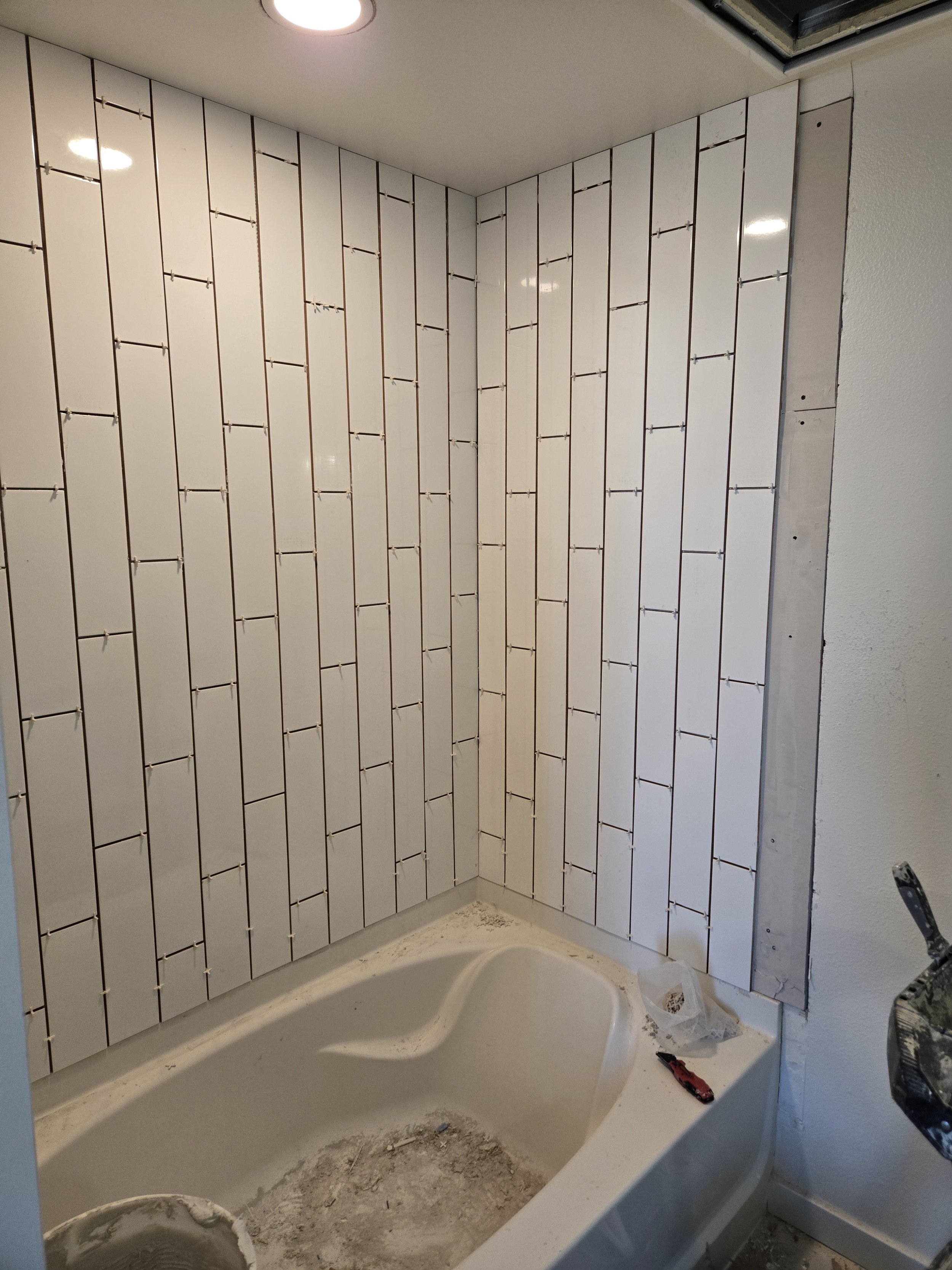 Bathroom with partially tiled wall, bathtub, and construction tools on the floor.