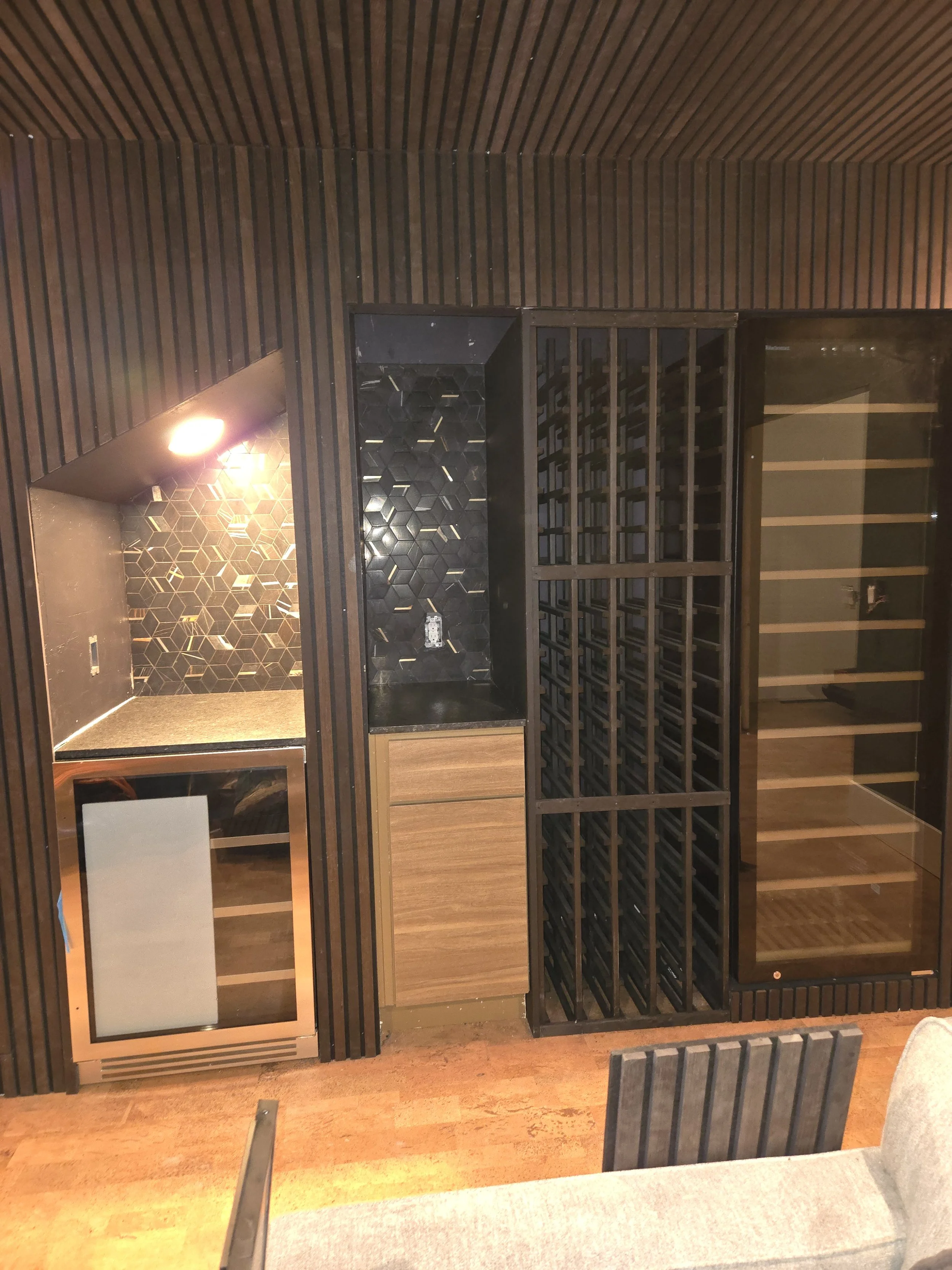 Interior of a wine cellar with wood paneling, a wine rack, a glass-door cabinet, and a shelf with a glass door, with a wooden floor.