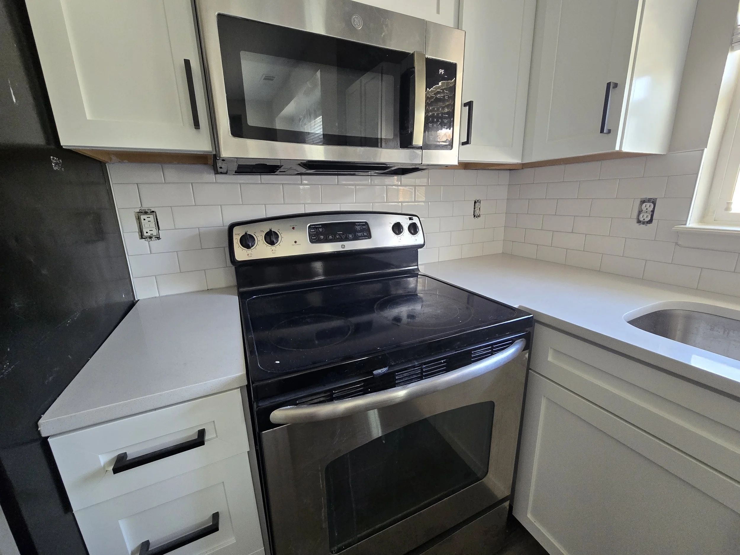 A kitchen with white cabinets, a black stove, a stainless steel microwave above it, and white subway tile backsplash.