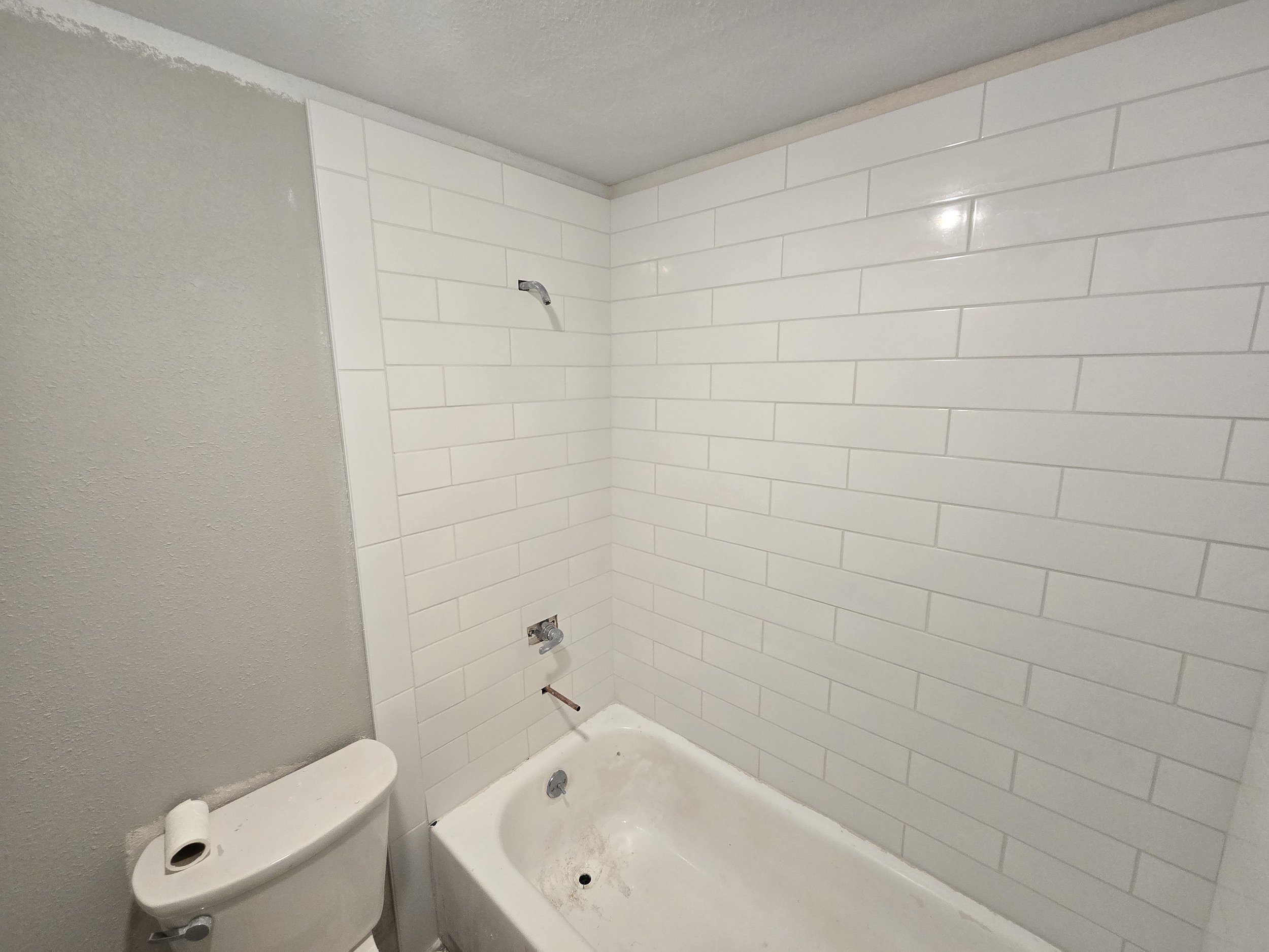 Bathroom shower with white subway tile walls, a bathtub, and a toilet with the seat down. The shower appears to be under construction or renovation.