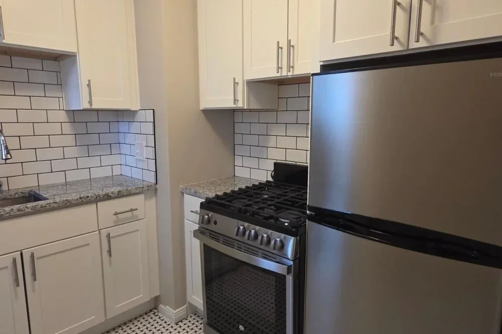 Kitchen with white cabinets, a granite countertop, a stainless steel stove, and a stainless steel refrigerator with white subway tile backsplash.