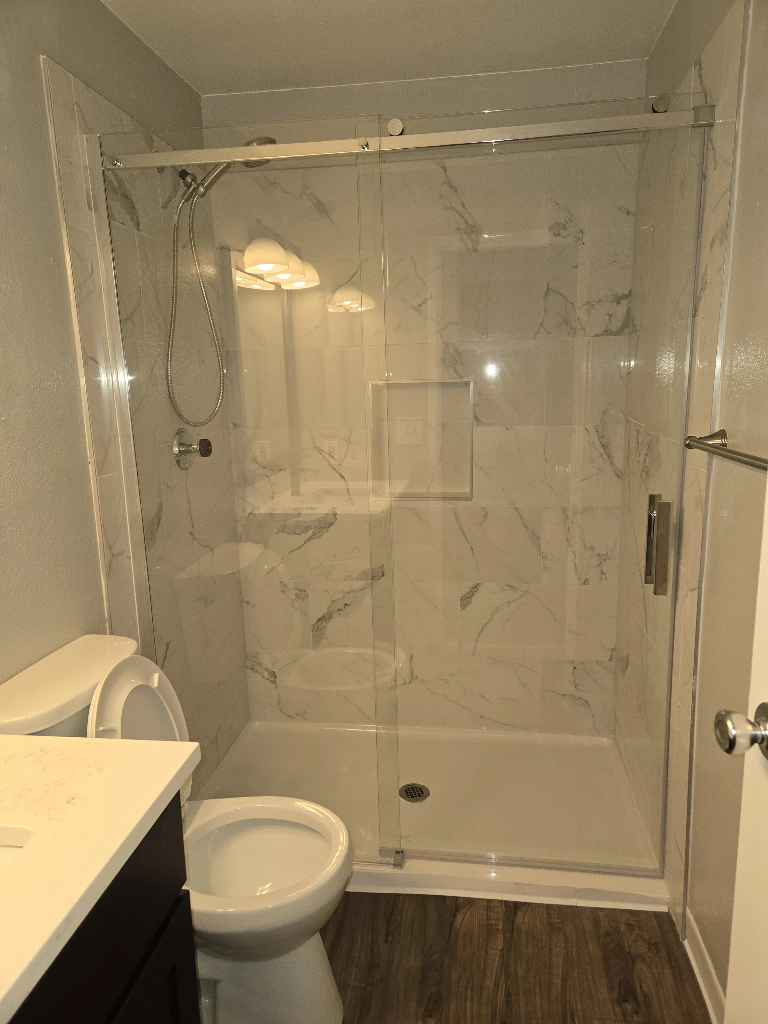 A small bathroom with a shower enclosure, a toilet, a sink with a black vanity, and a marble wall in the shower area.