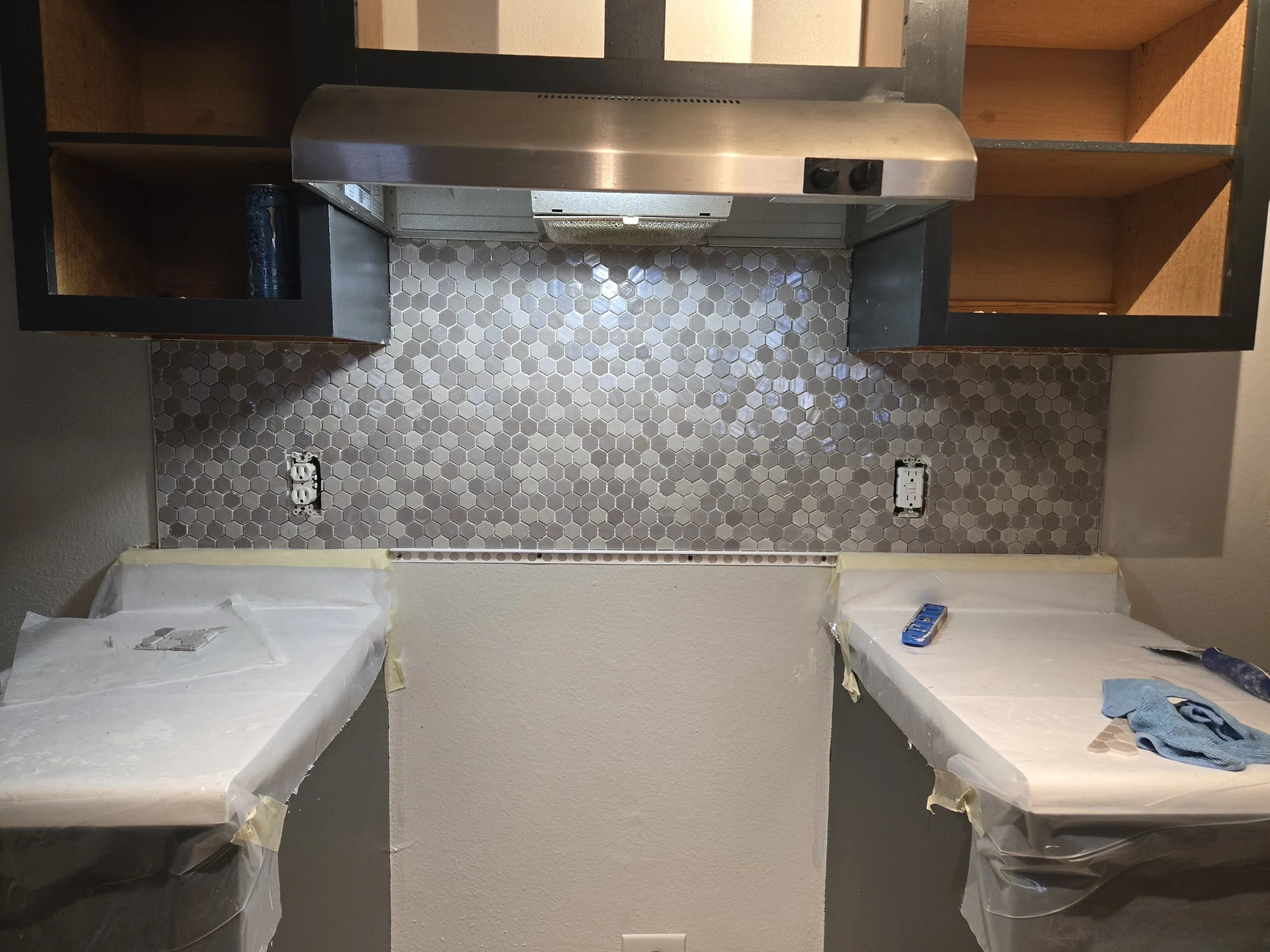 Kitchen wall with honeycomb tile backsplash, countertop covered with protective paper, and electrical outlets being installed.