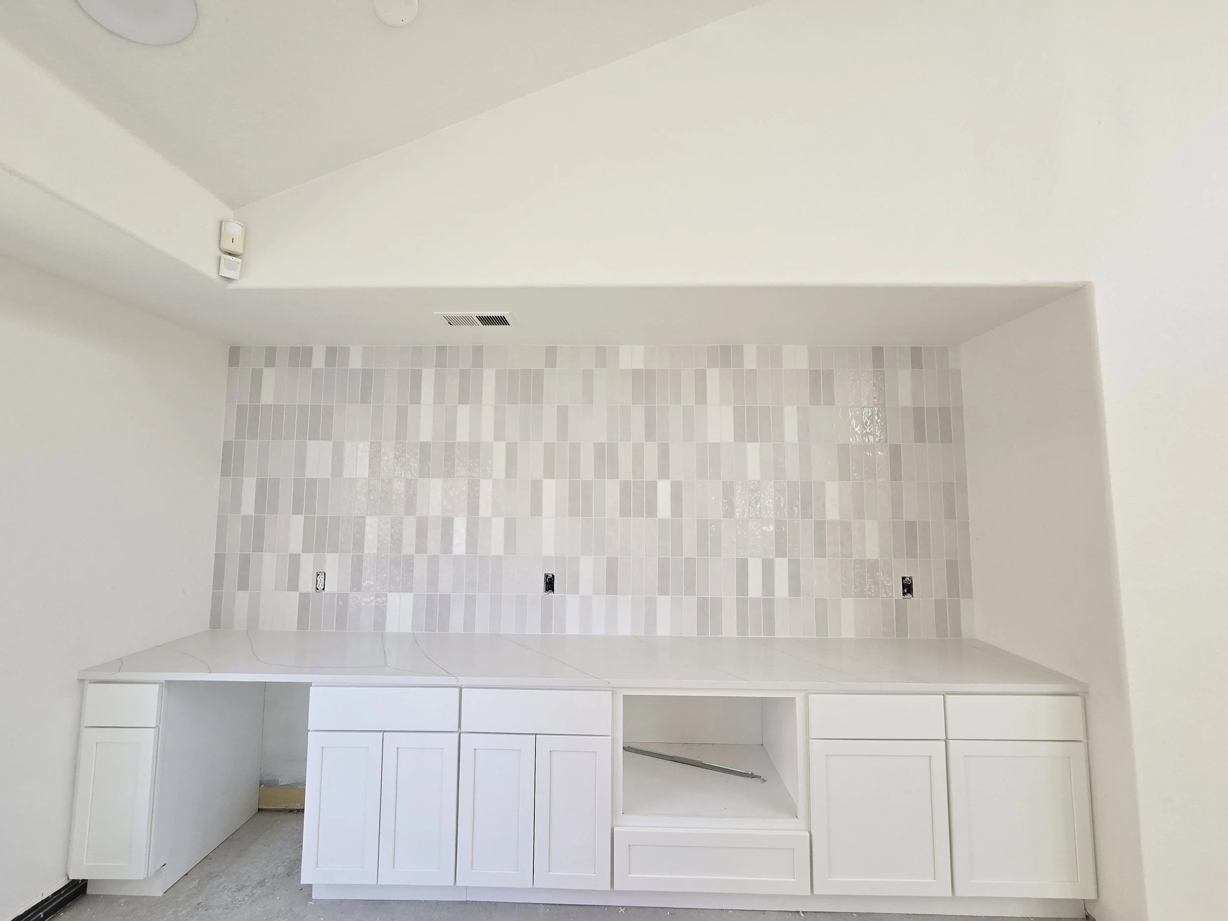 Empty kitchen space with white cabinets, tiled backsplash, and a vent in the ceiling.