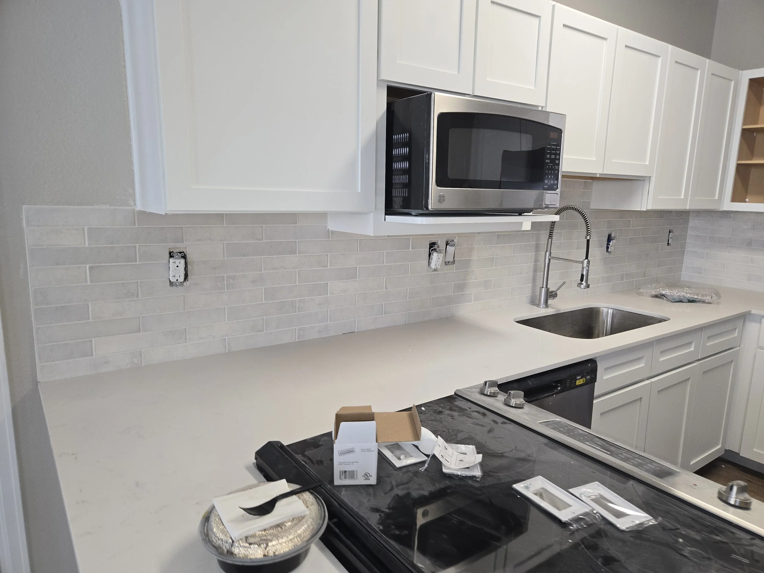 Kitchen with white cabinets, a stainless steel microwave, a sink, and a black stove. There are some tools and packaging on the countertop, indicating ongoing renovations or installation.
