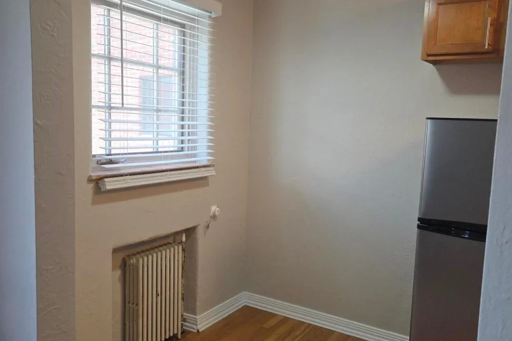 Empty kitchen corner with window, radiator, and refrigerator.